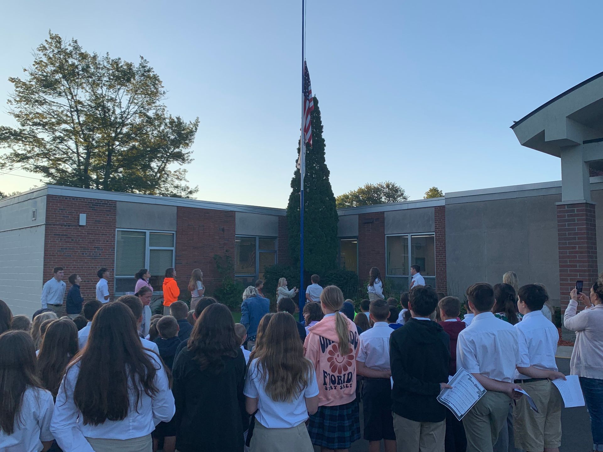 A group of classrooms standing outside looking at the American flag.