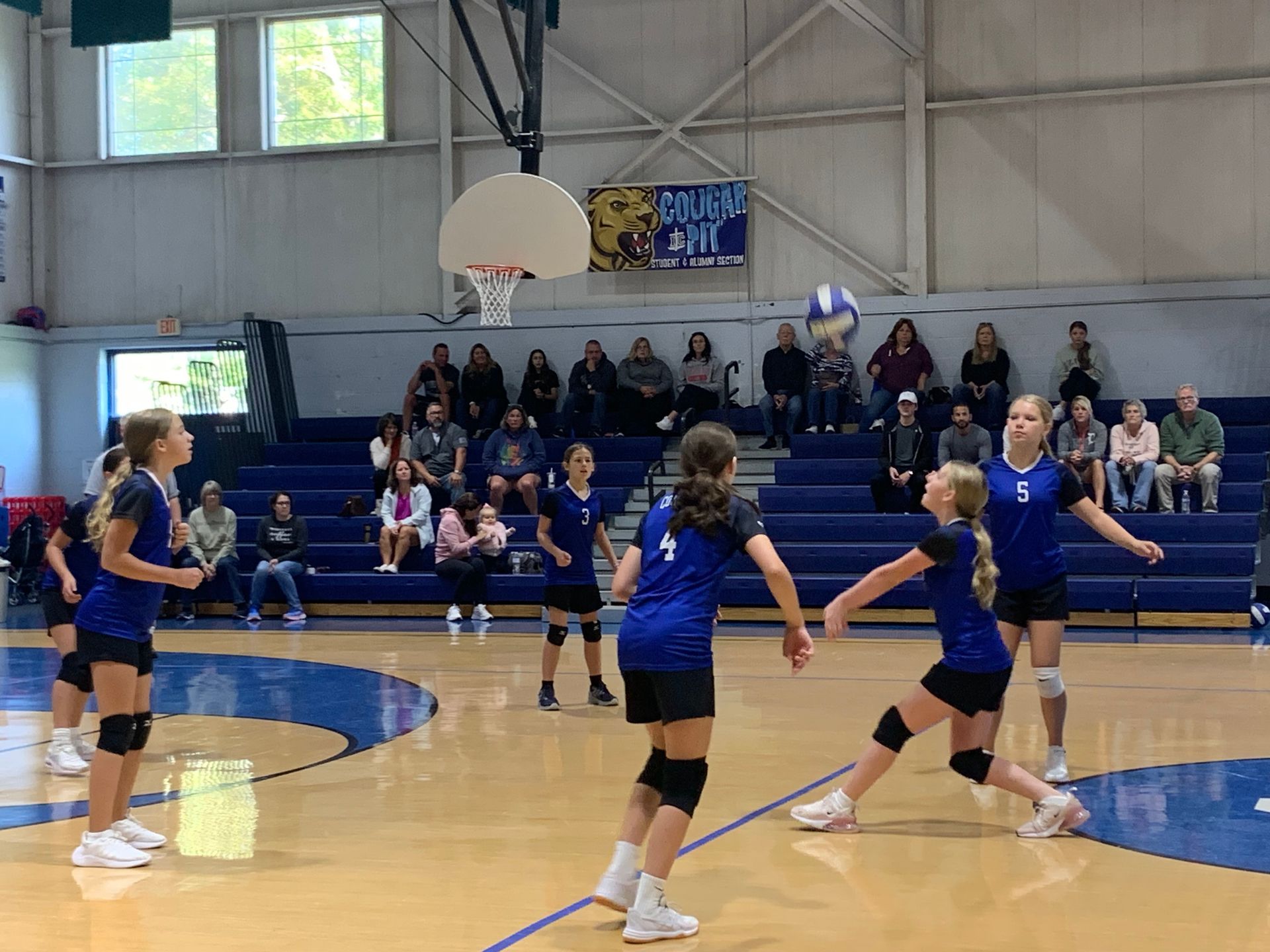 Girls playing volleyball in front of a cougar gym sign.