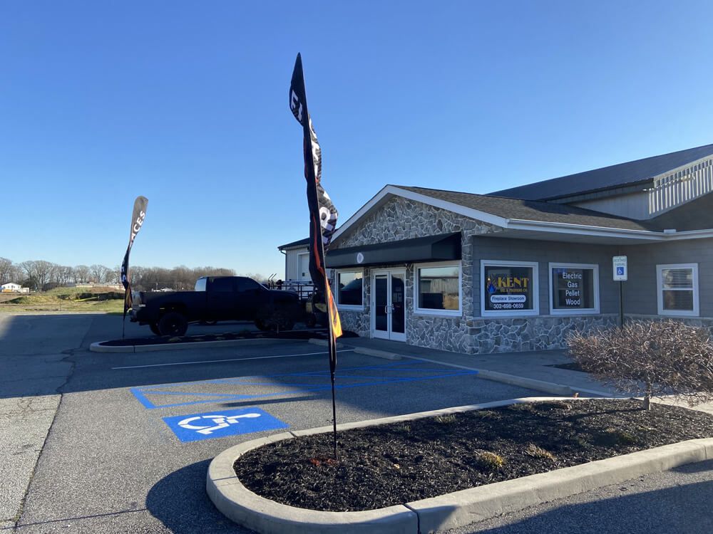 Accessible parking spaces outside a gray storefront with a black truck and feather flags.