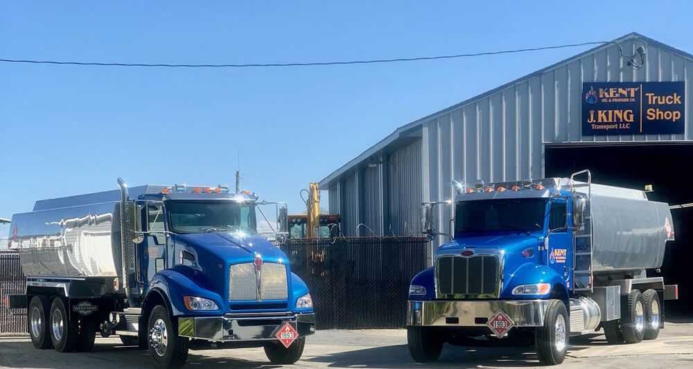 Two blue dump trucks parked outside a truck shop on a sunny day