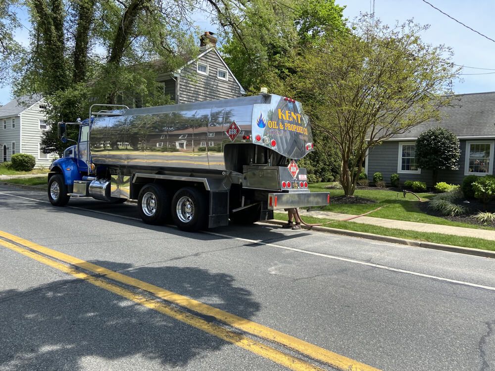 Chrome tanker truck parked on a residential street beside a sidewalk and trees