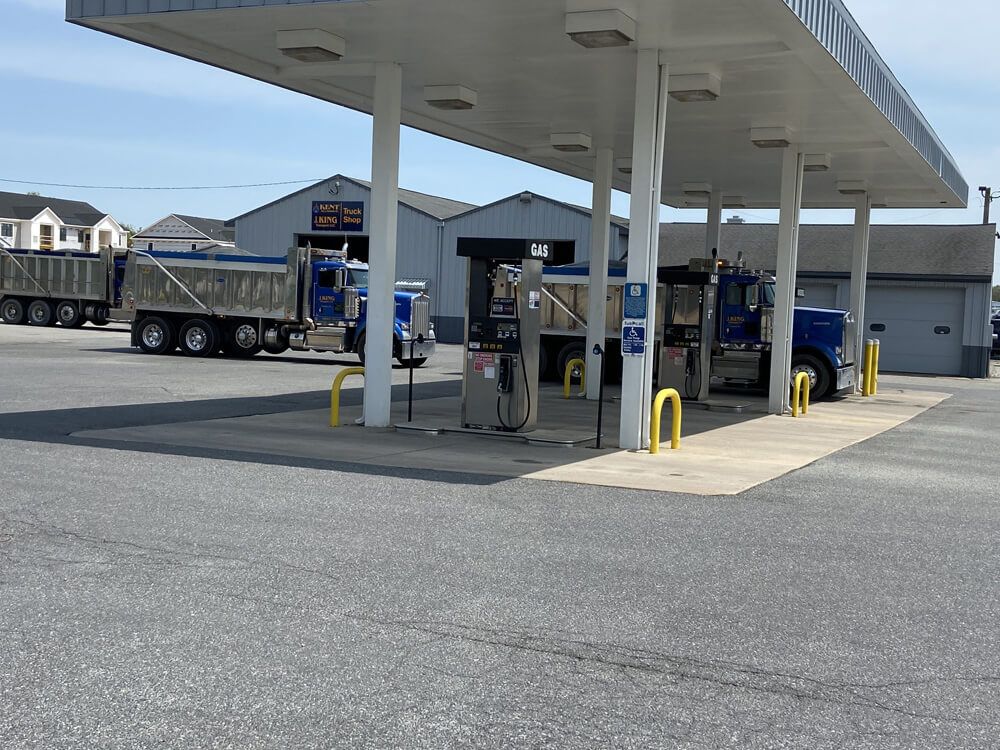 Gas station canopy with fuel pumps, a blue semi-truck, and a building in the background
