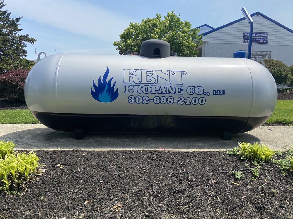 Silver propane tank labeled “KENNETH PROPANE CO.” on a lawn outside a building