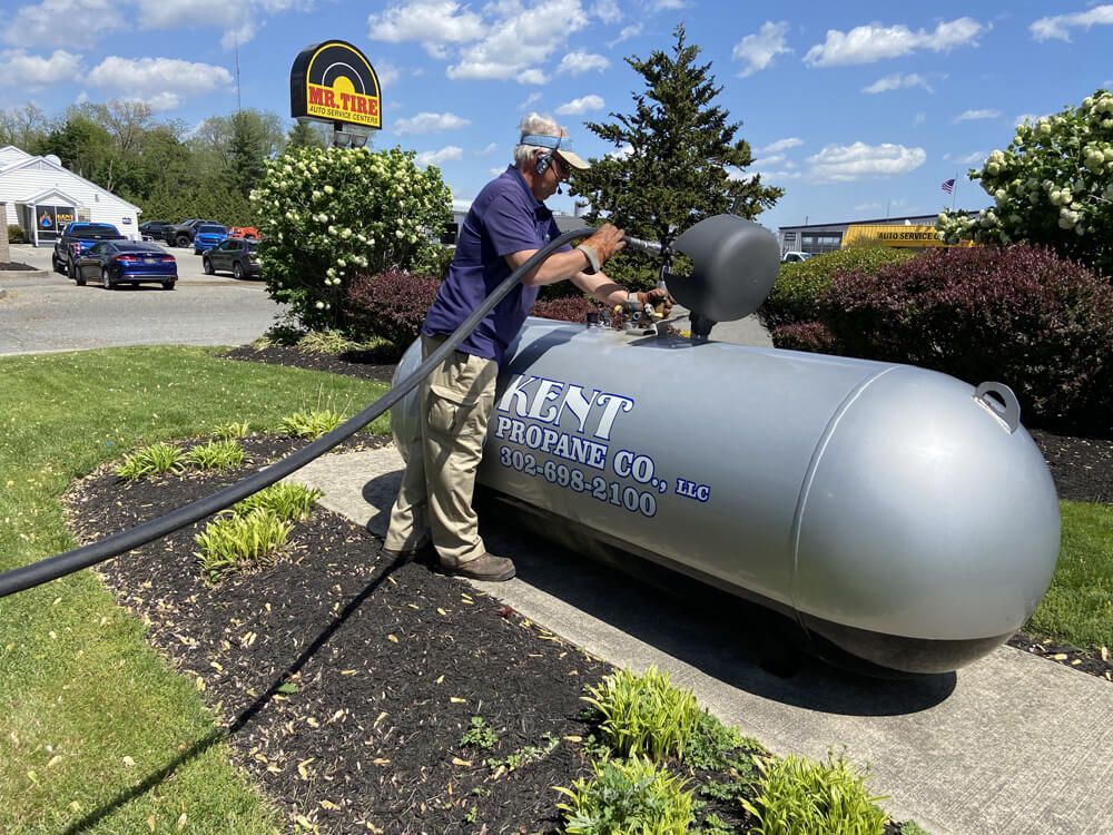 Worker filling a gray propane tank with a hose outside a business on a sunny day