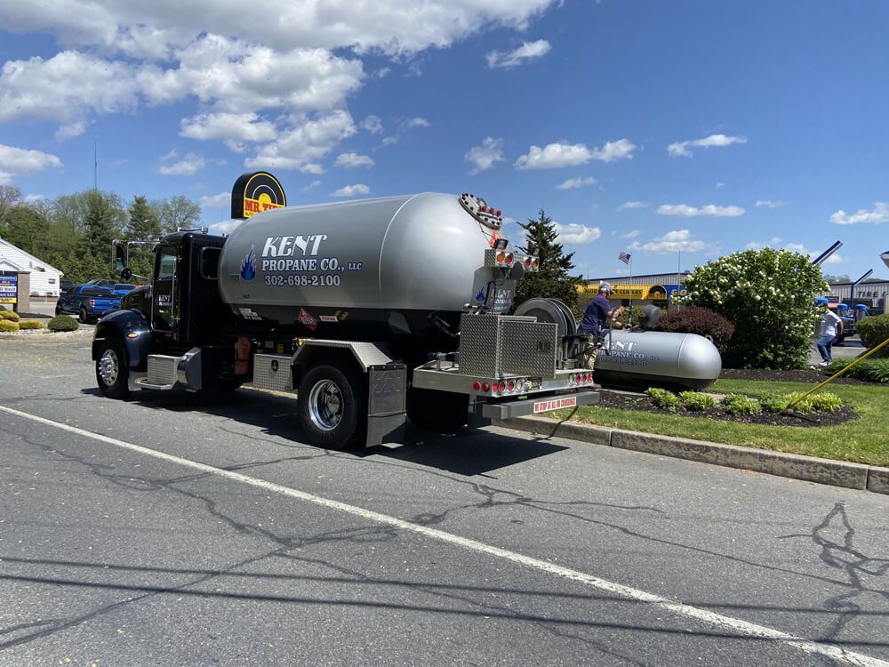 Silver tanker truck parked by a roadside garden on a sunny day