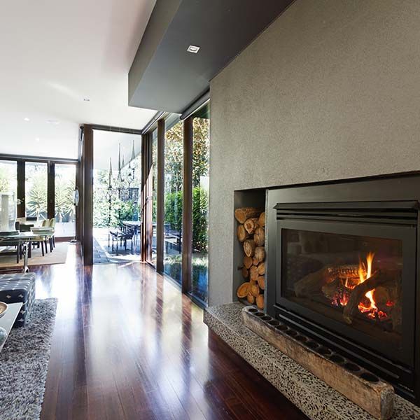 Modern living room with fireplace, dark wood floor, and floor-to-ceiling windows opening to a patio