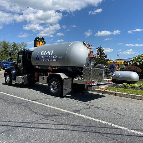Silver BEST septic truck parked by a road with a small tank trailer and blue sky behind it