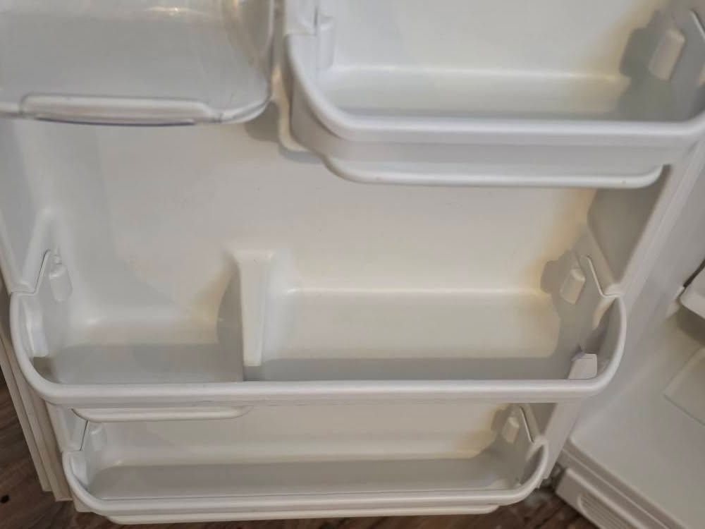 Open refrigerator door with empty white shelves and bins