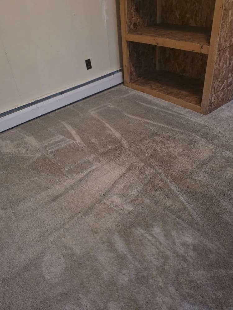 Carpeted room corner with white baseboard, beige wall, and empty wooden shelving unit