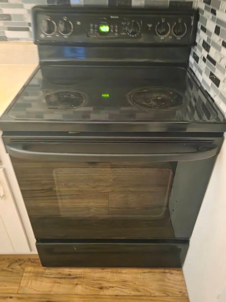 Black electric stove with oven in a kitchen, showing the control panel and burners.