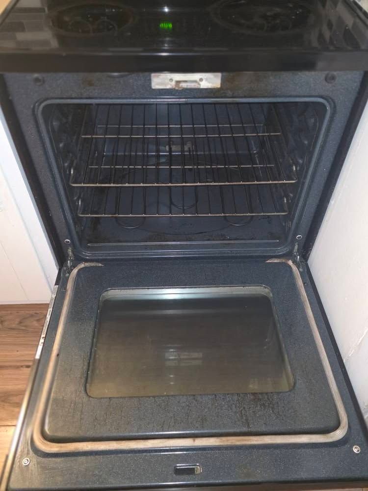 Open oven with dark interior and metal racks, showing the oven door and baking tray holder.