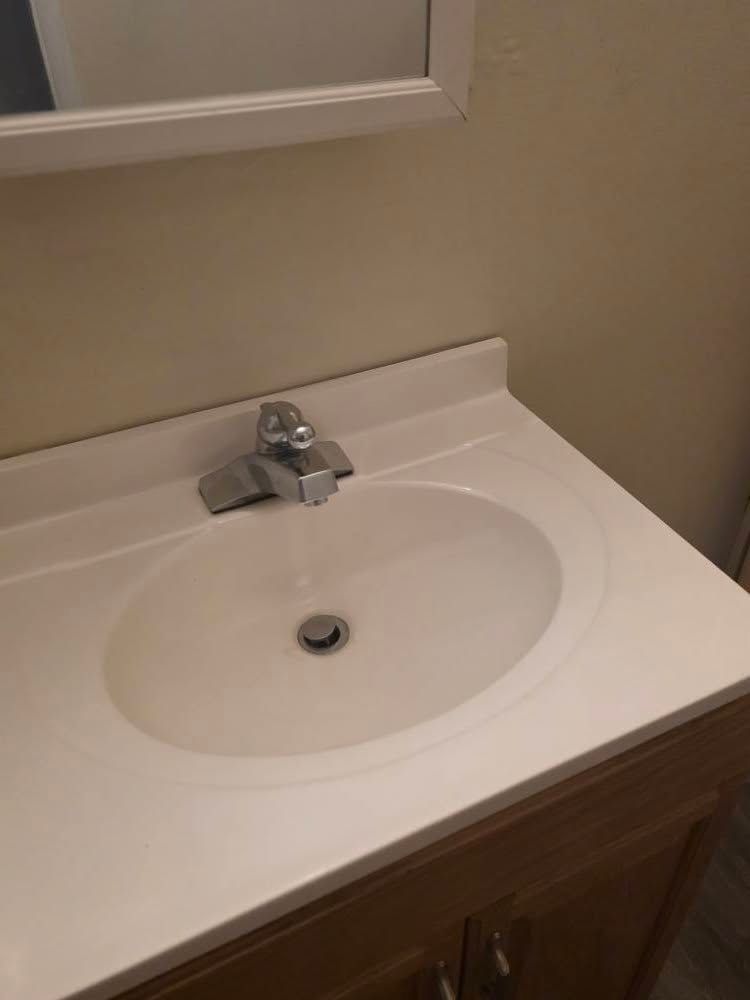 Bathroom vanity with white sink, chrome faucet, and mirror above wooden cabinet