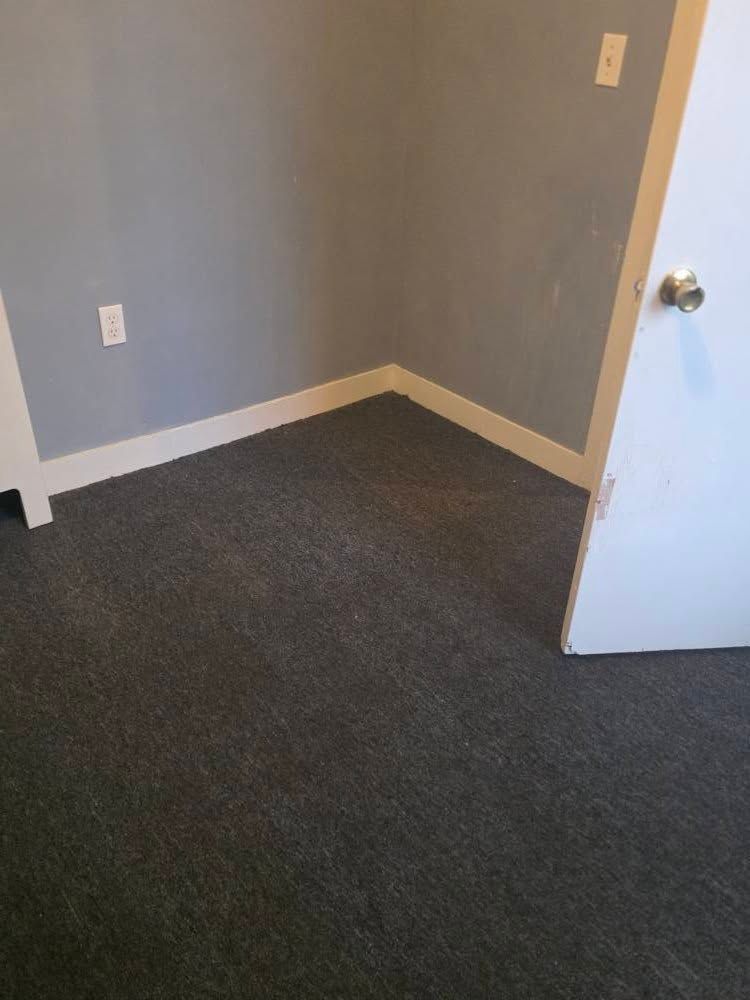 Empty carpeted room with gray walls, white trim, and an open door