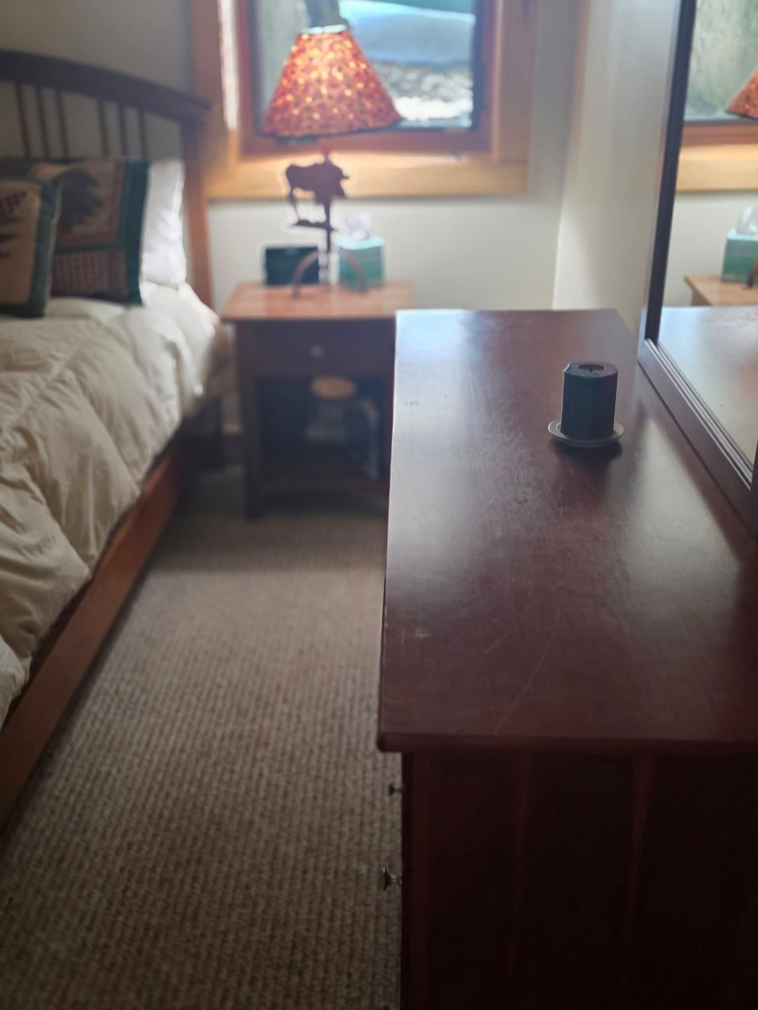 Bedroom with bed, nightstand lamp, and wooden coffee table on a carpeted floor.