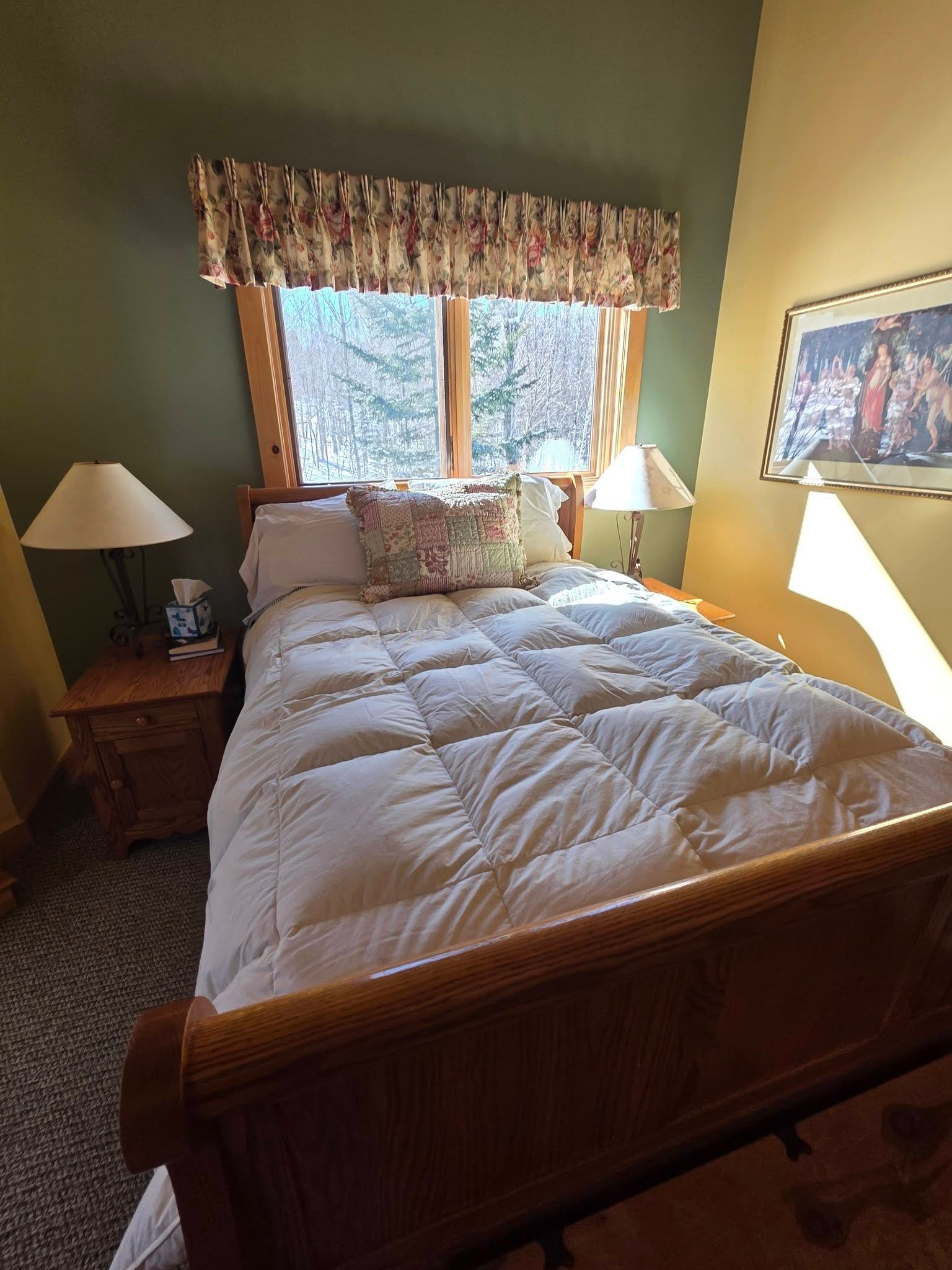 Bedroom with a wooden bed, white comforter, bedside lamps, and a window with patterned valance.