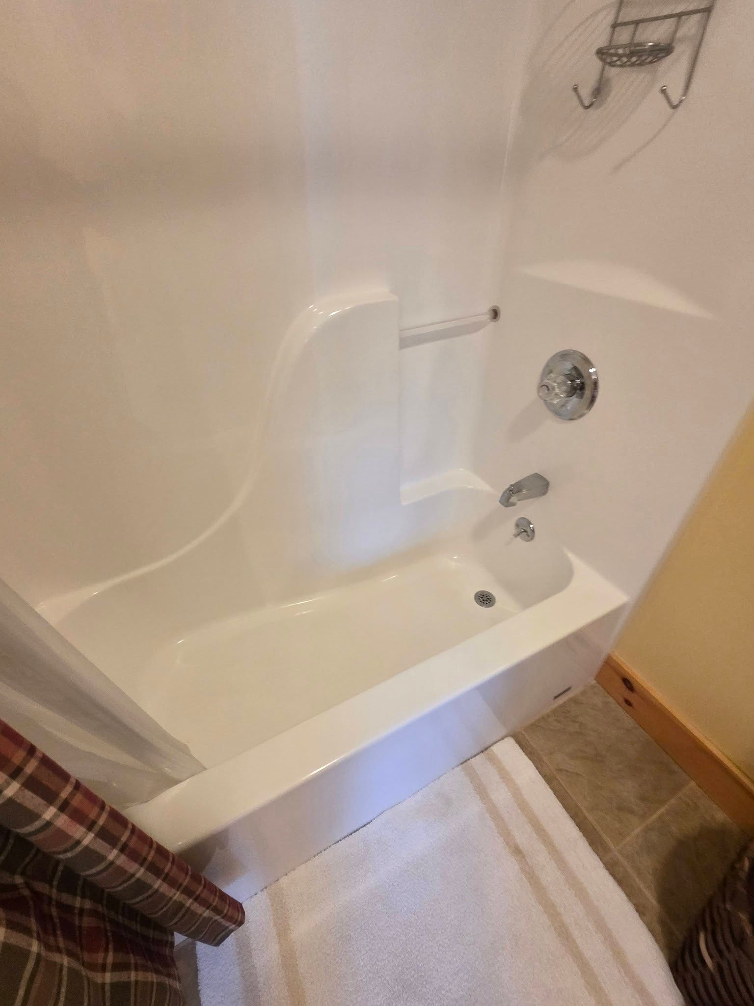 White bathtub with shower in a small bathroom, next to a beige rug and curtain