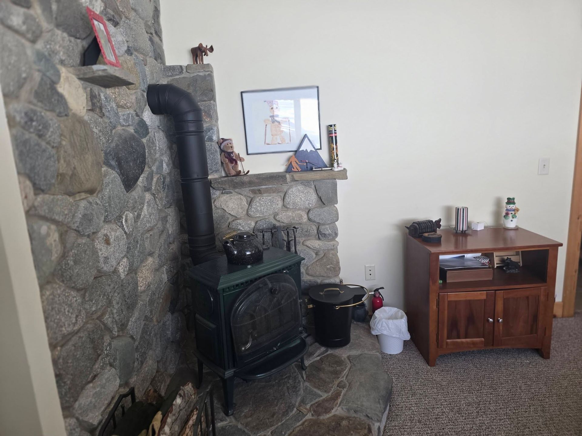 Living room with stone fireplace, black wood stove, and wooden side table with decor