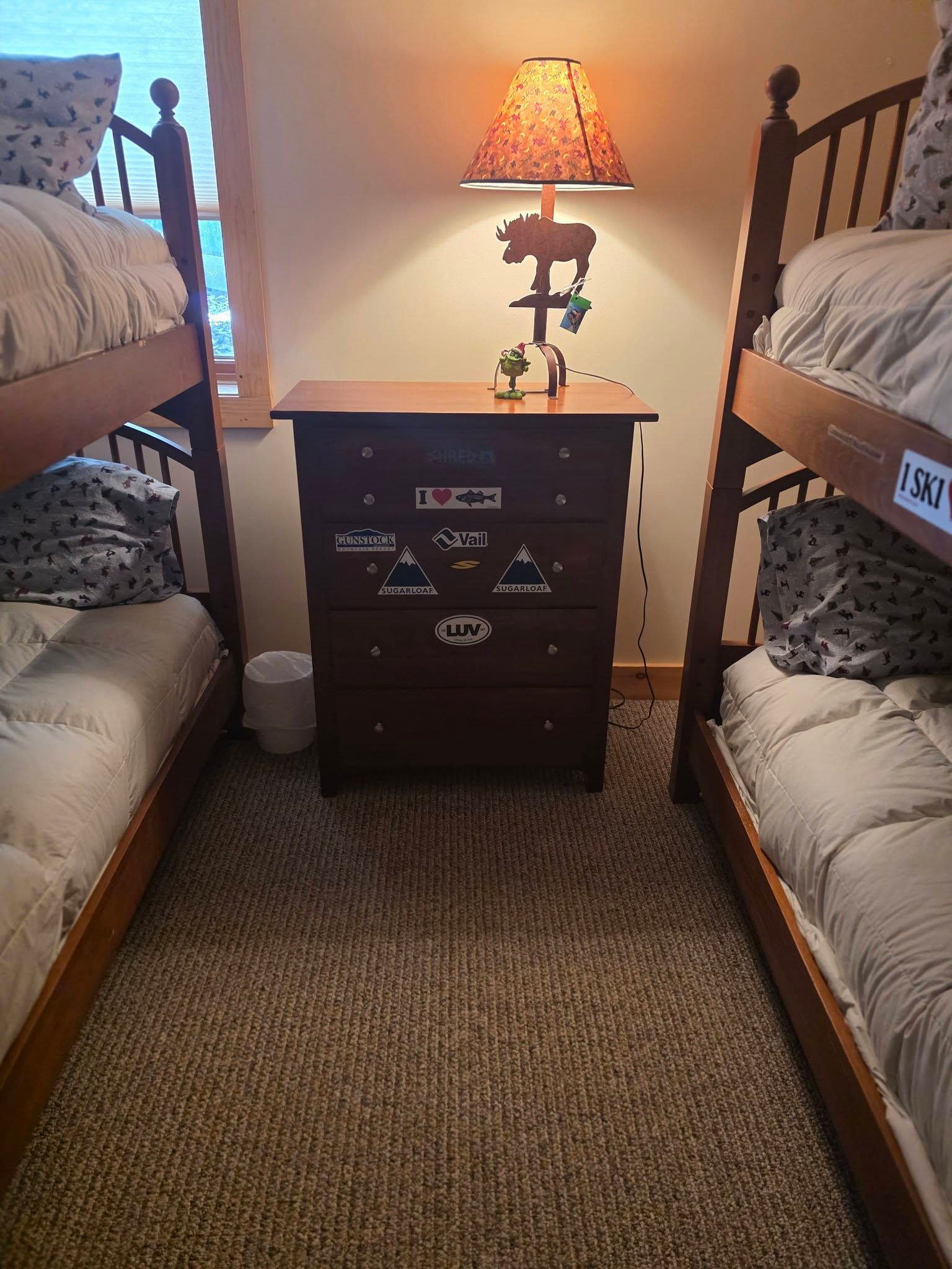 Dorm-style room with bunk beds flanking a dark nightstand and glowing lamp on a woven rug.