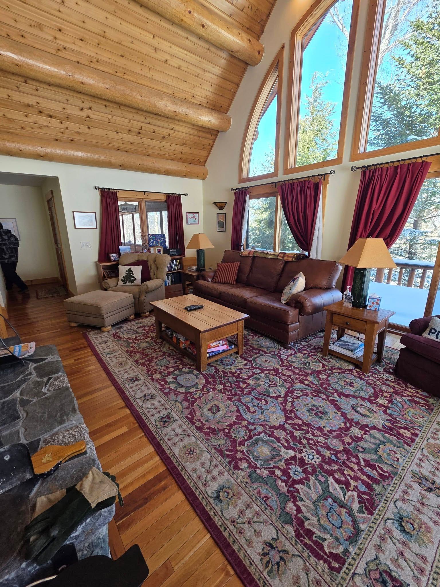 Cozy living room with stone fireplace, leather sofas, red rug, and large windows with red curtains