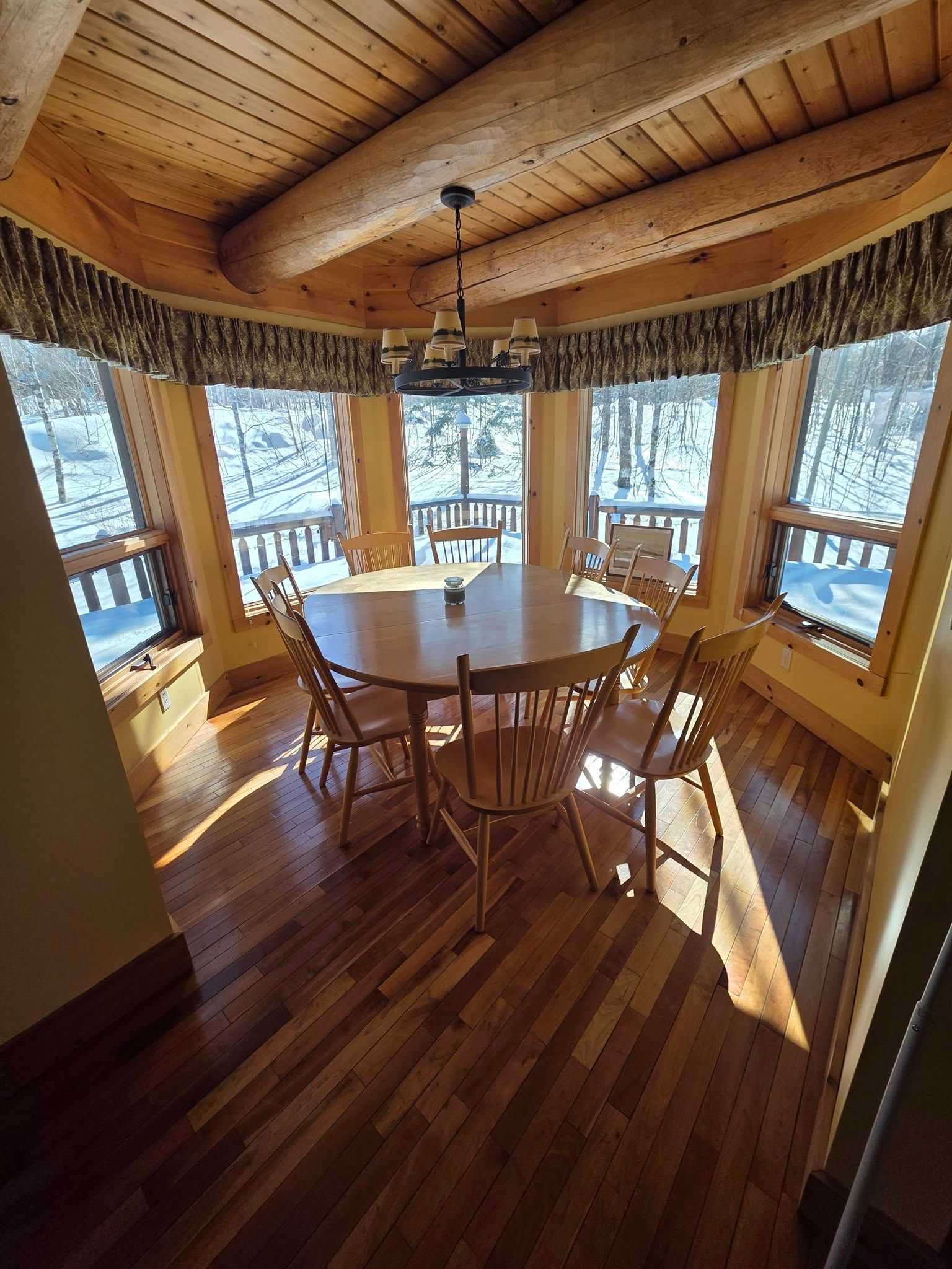 Wood-paneled dining nook with round table and chairs, sunlit windows overlooking water.