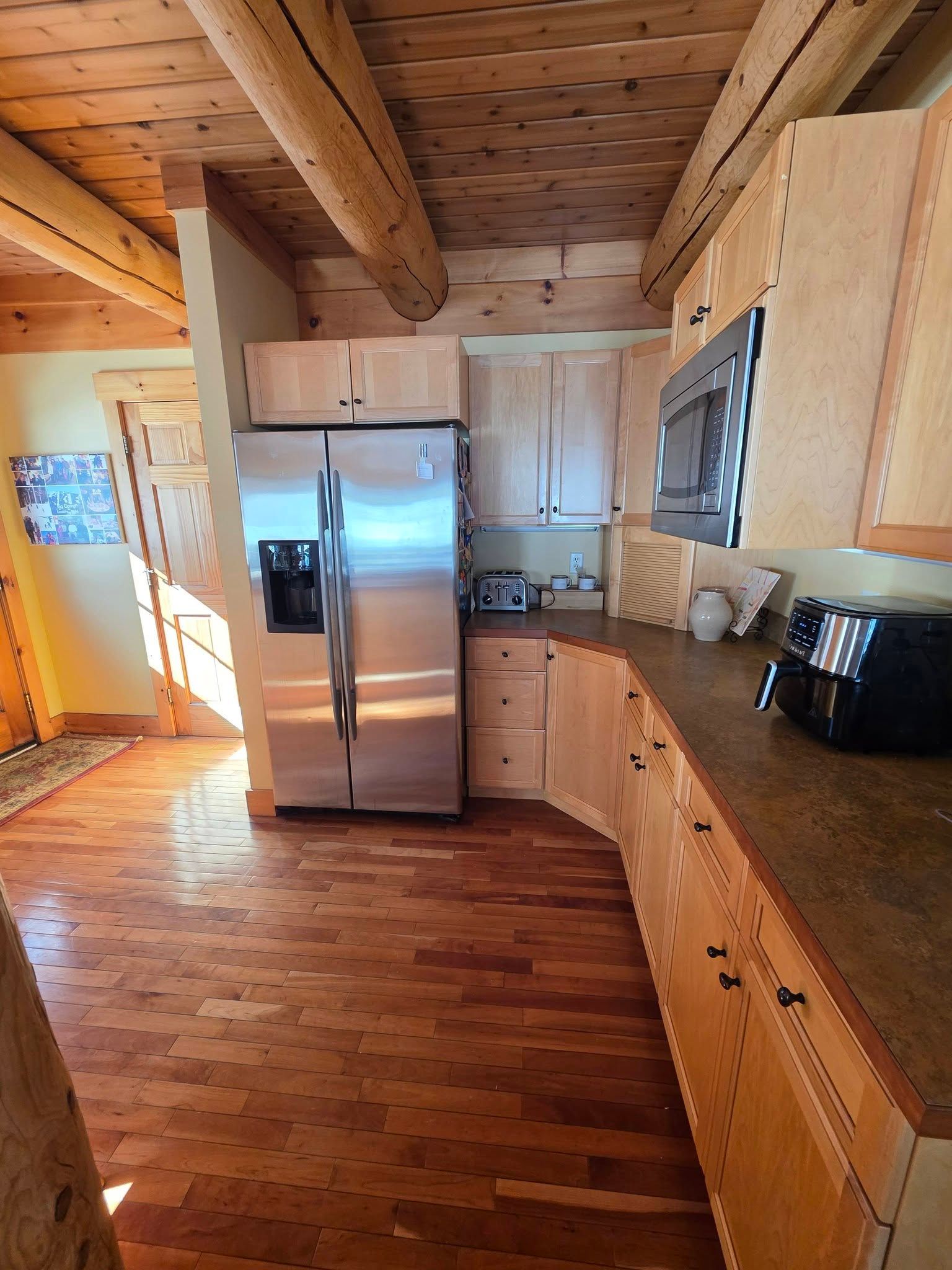 Rustic kitchen with wood beams, stainless fridge, and wooden cabinets under warm light.