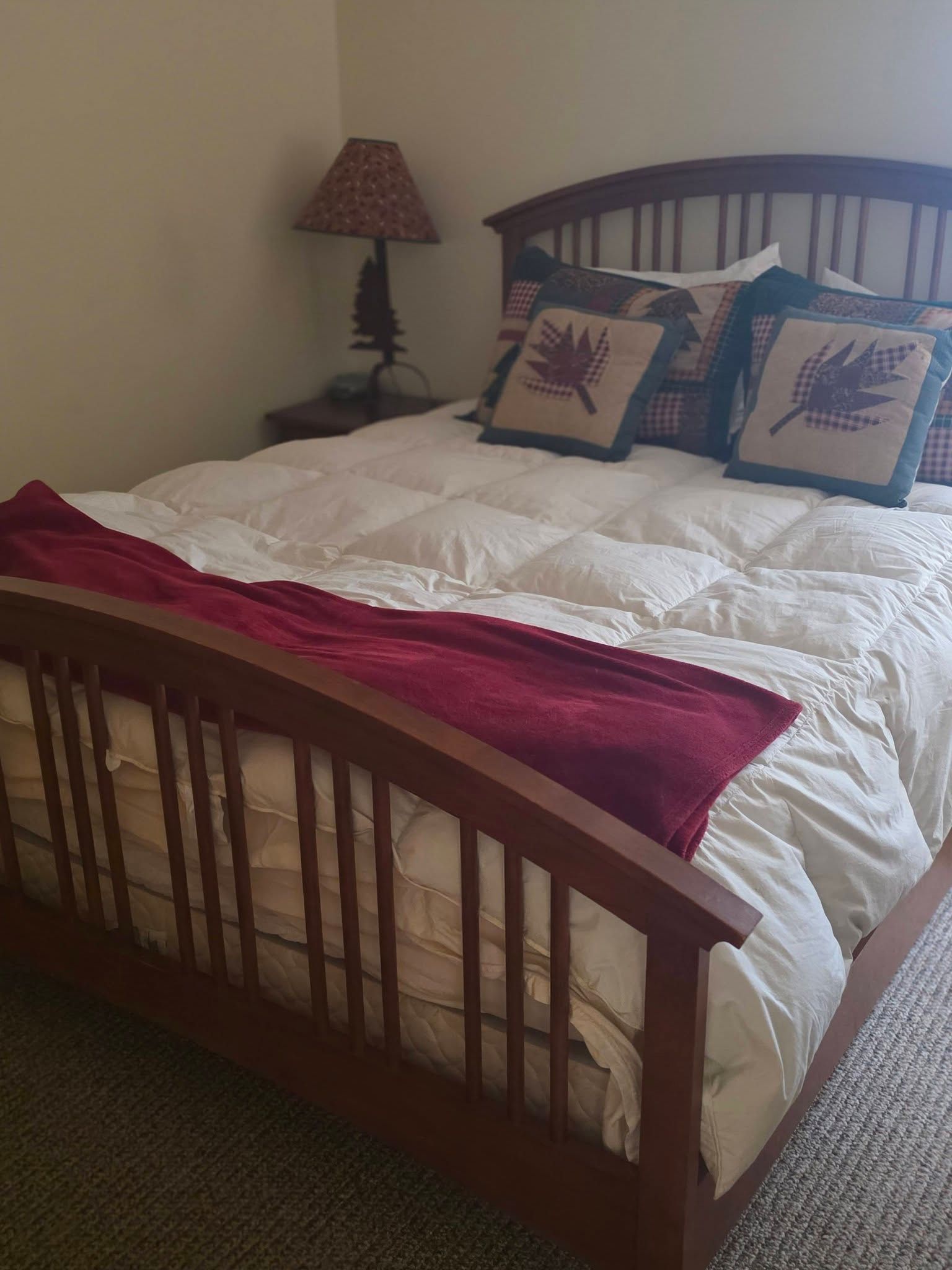 Bedroom with a wooden bed, white quilt, red throw, and bedside lamp against beige walls