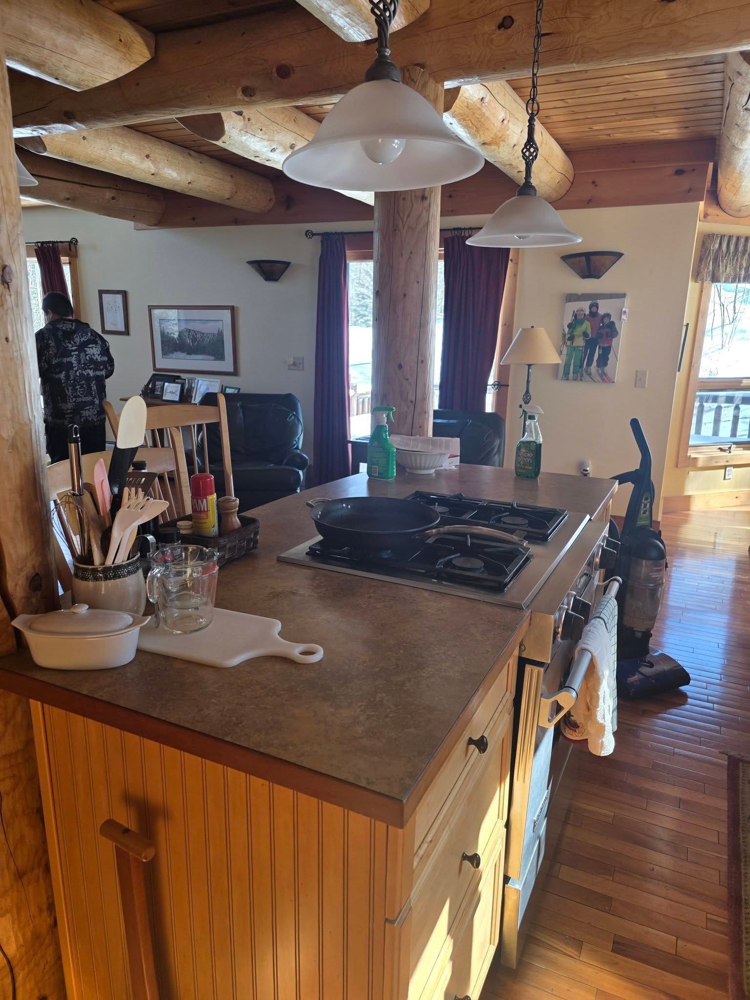 Rustic kitchen with wood beams, island, stove, and sunlight through windows