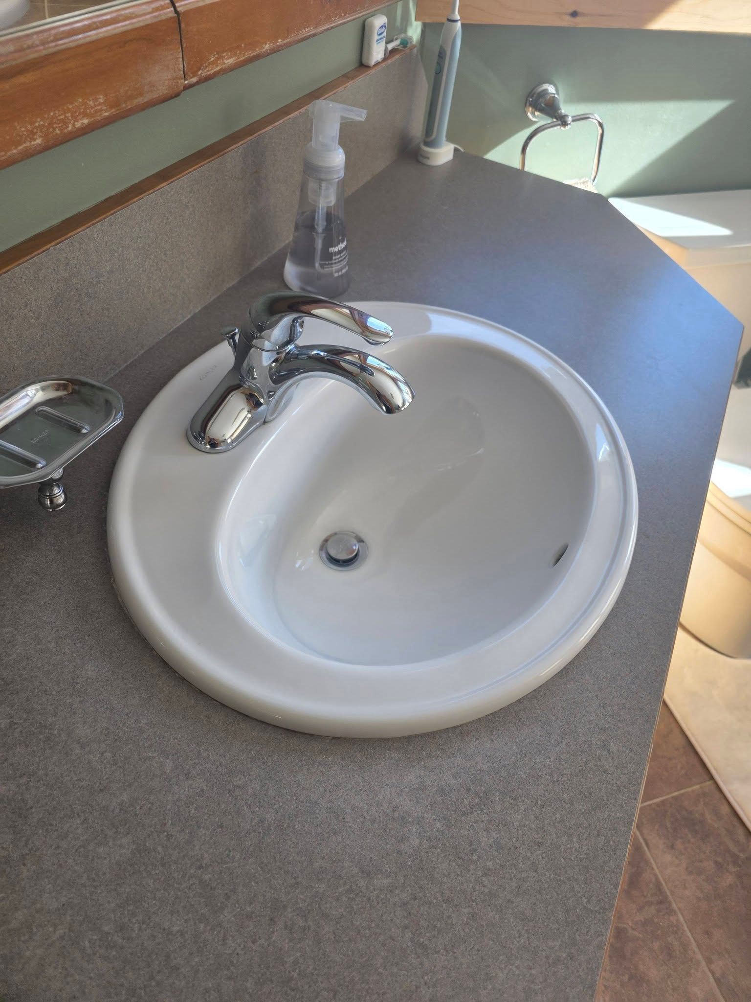 Bathroom sink with chrome faucet on a gray countertop next to a mirror and soap dispenser