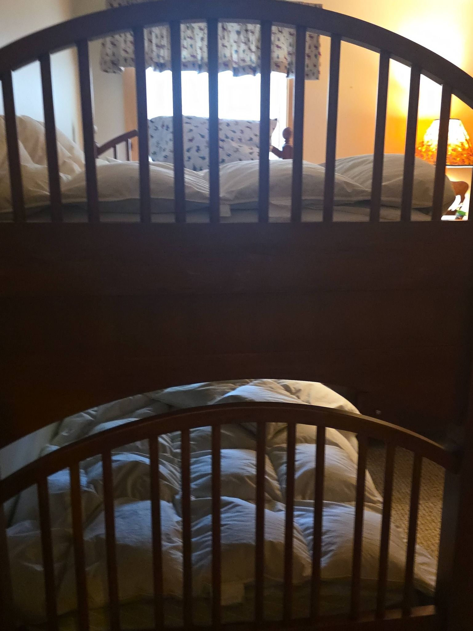 Dim bedroom with two wooden beds, one on top of the other, lit by warm light from the right.