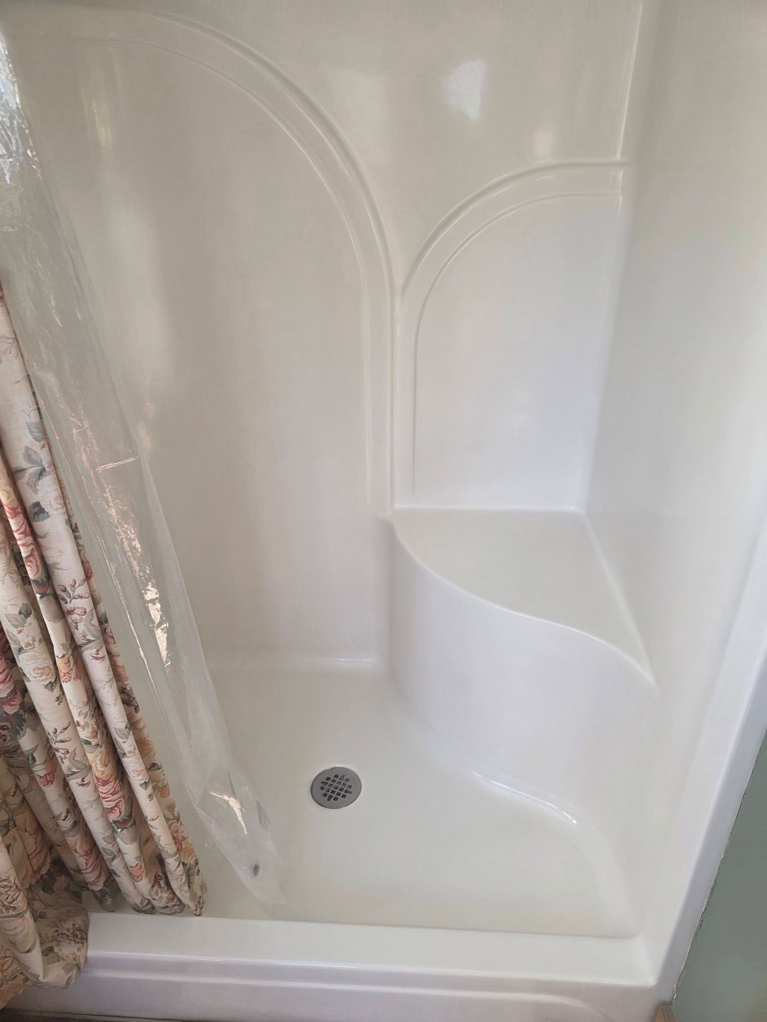 White shower stall with curtain, built-in seat, and drain visible.