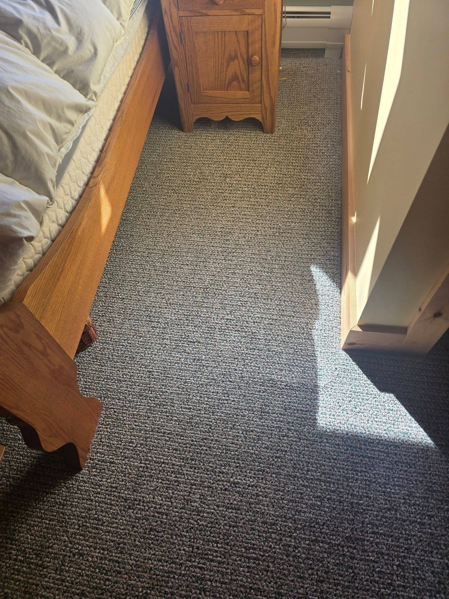 Bedroom corner with patterned carpet, wooden bed frame, nightstand, and bright sunlight on the floor