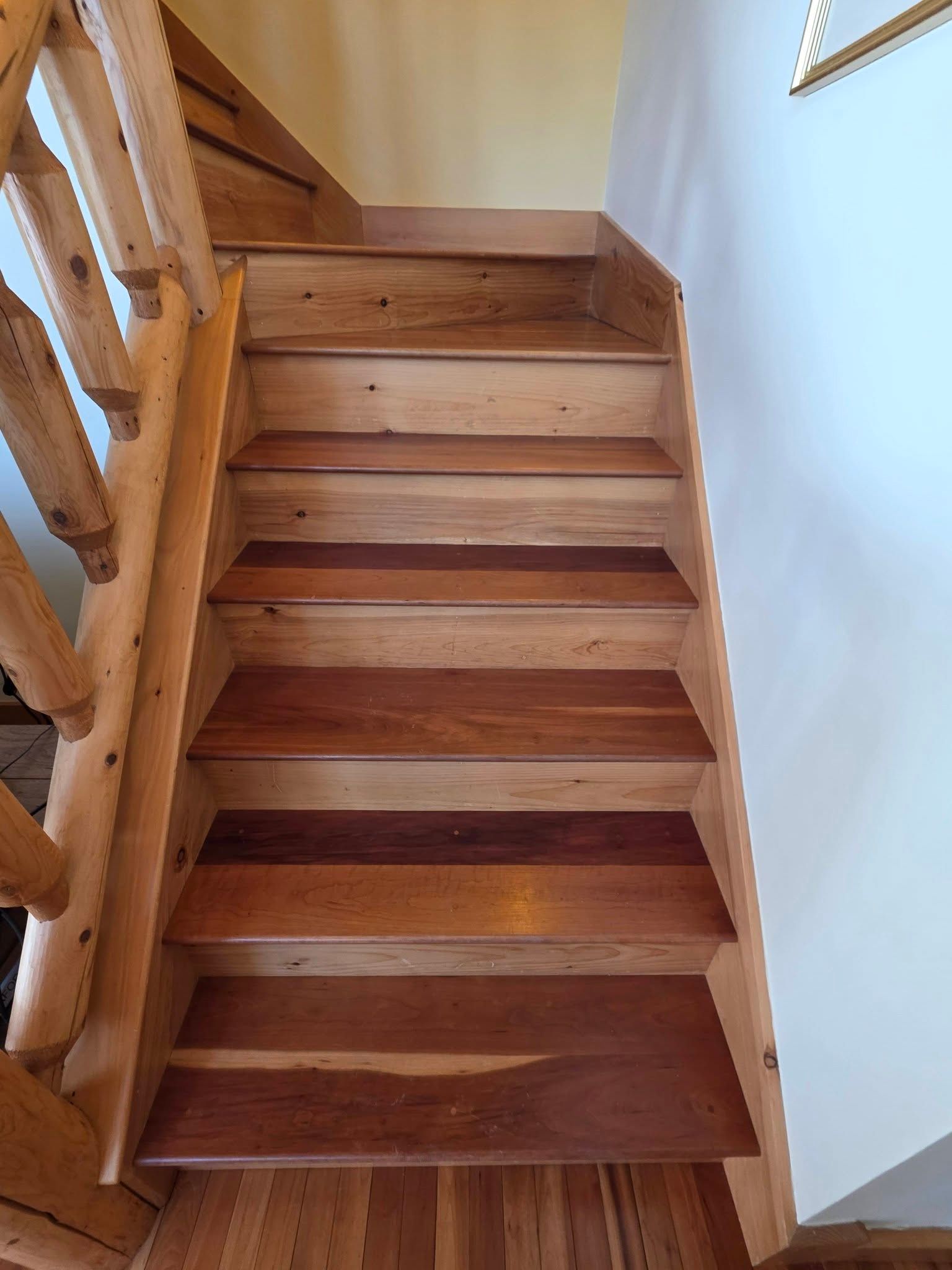 Wooden staircase with dark treads and a white wall beside a rustic railing.