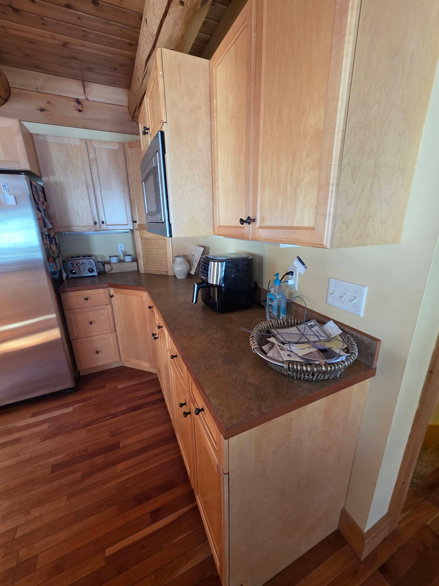 Narrow wood-paneled kitchen with stainless fridge, countertop appliances, and hardwood floor