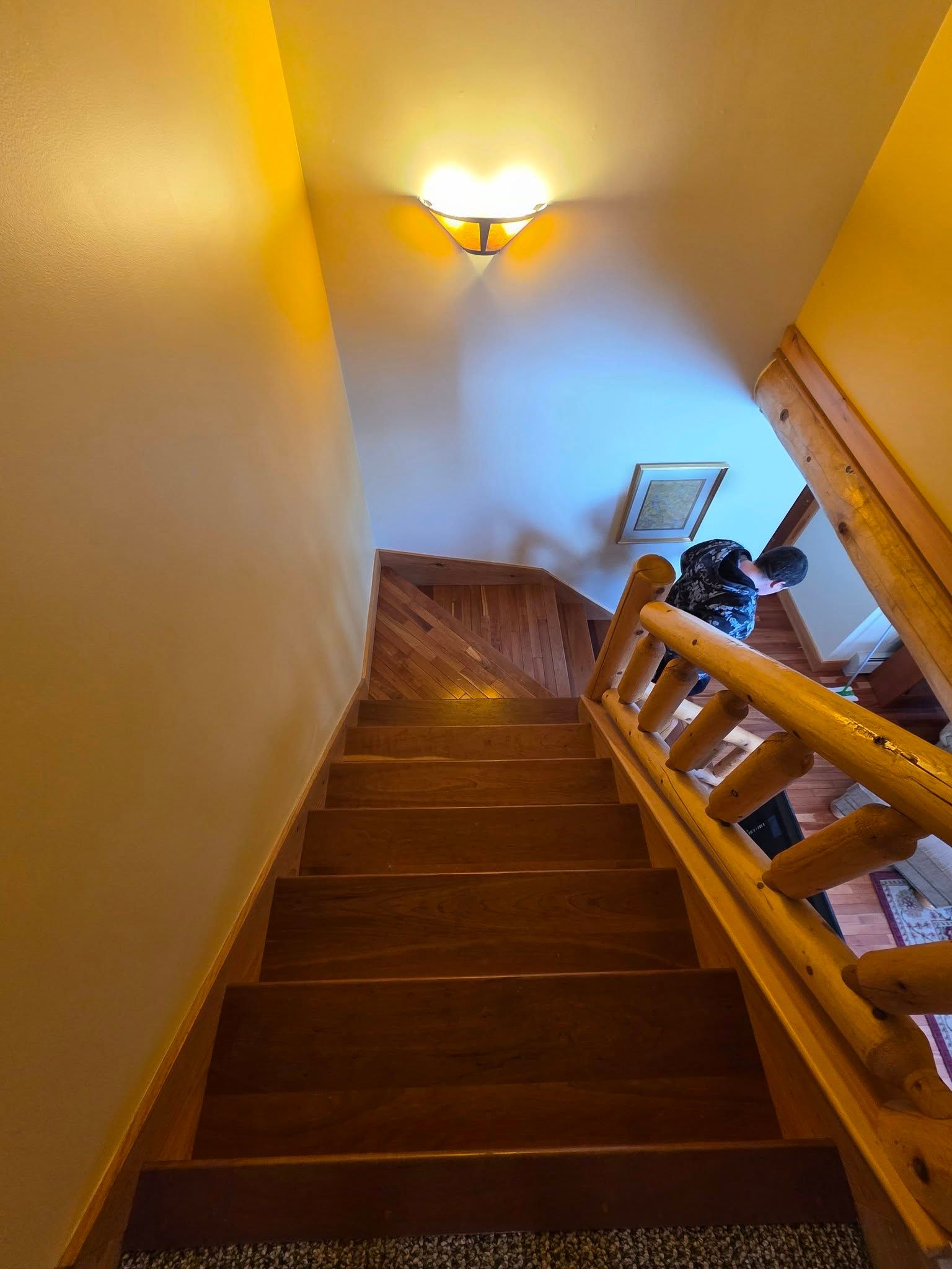 Wooden staircase with railing in a warmly lit home, viewed from the top looking down.