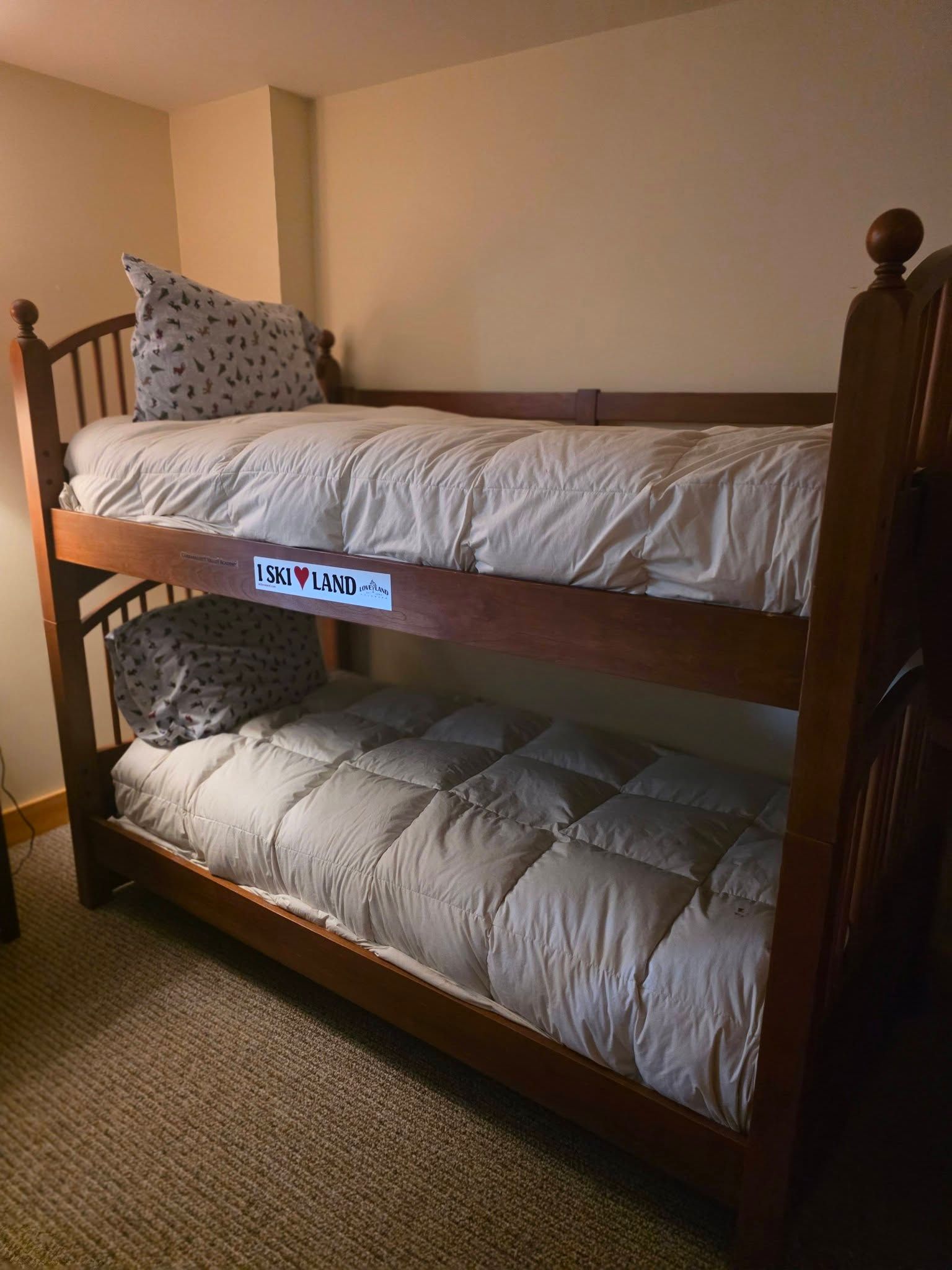 Wooden bunk bed with gray bedding and a patterned pillow in a carpeted bedroom