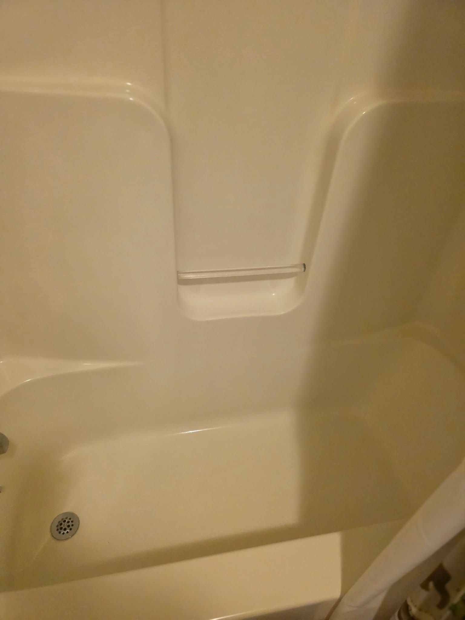Empty beige bathtub with built-in grab bar and drain.