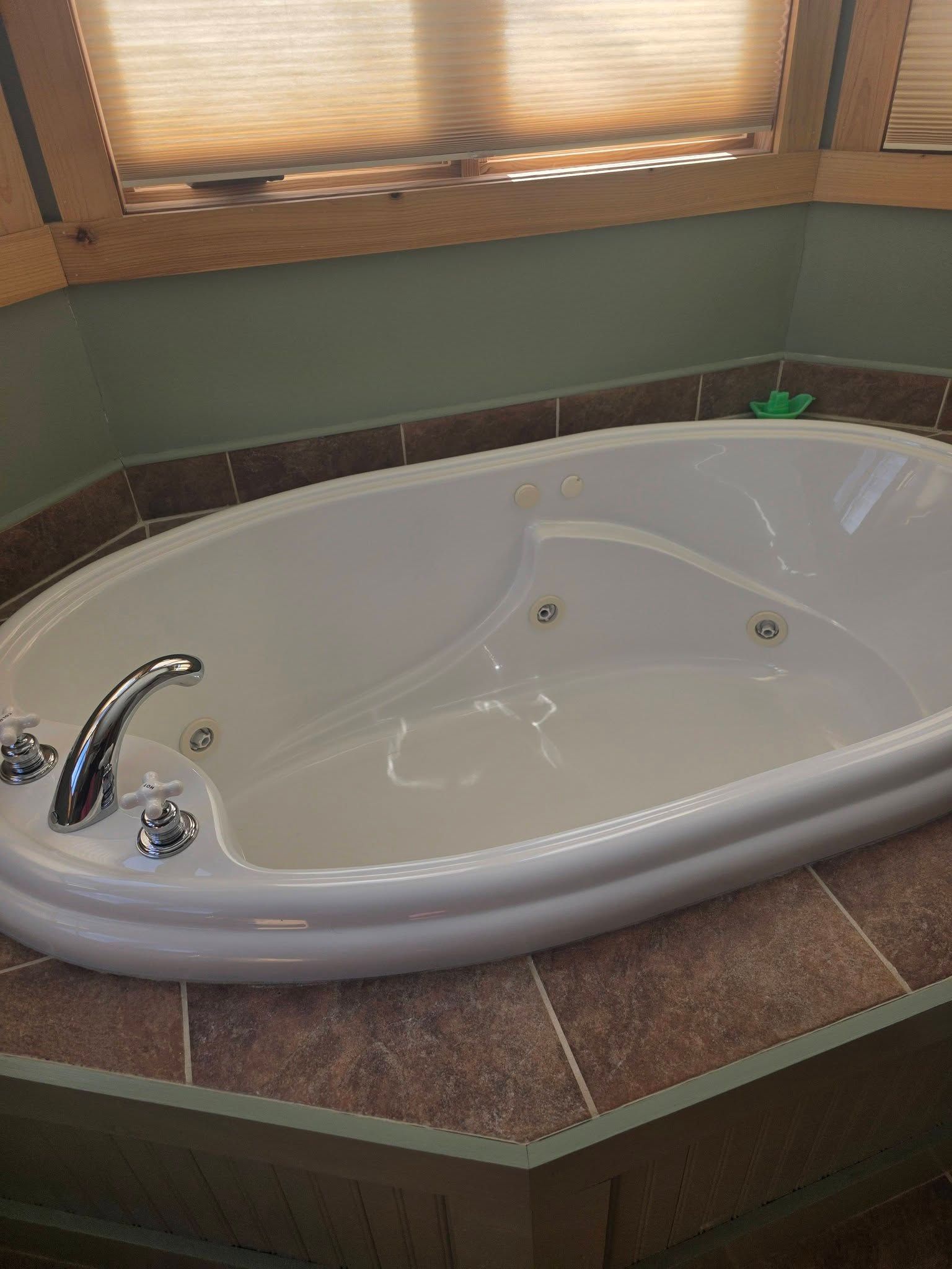 Corner bathtub in a tiled bathroom with a chrome faucet and a window above it.
