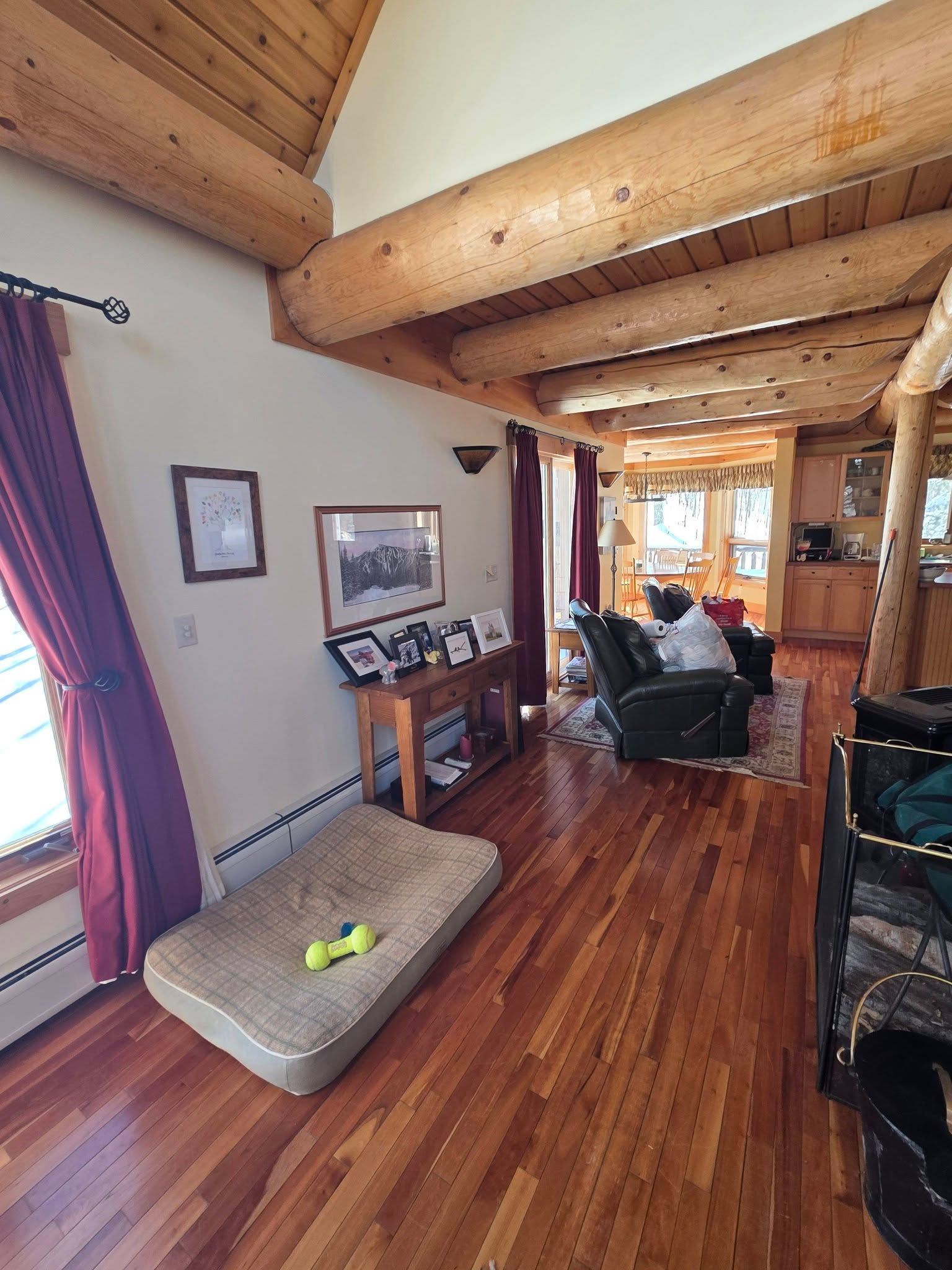 Cozy living room with wood beams, purple curtains, framed art, and a cat bed on the floor.