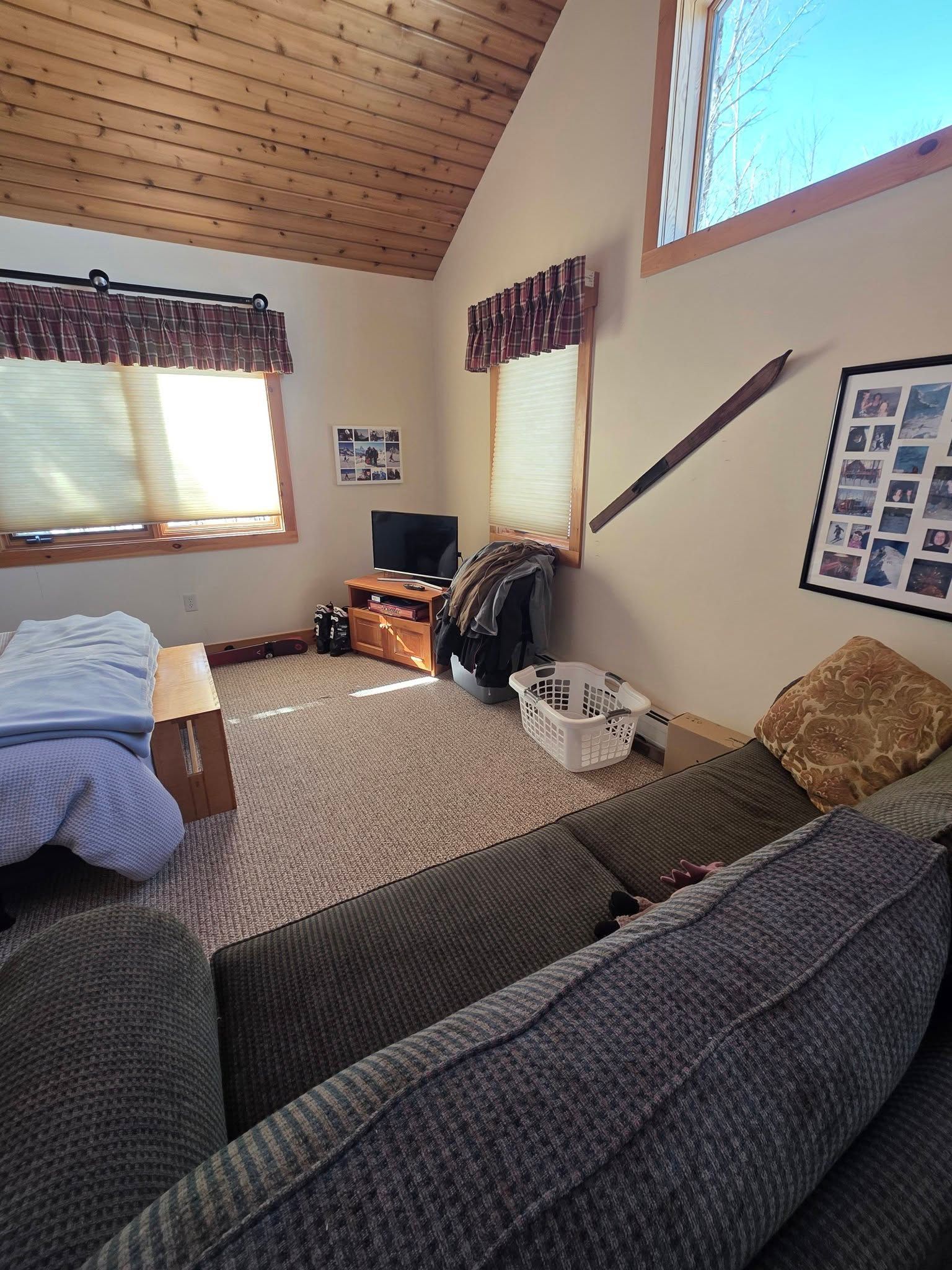 Cozy bedroom with wood ceiling, two windows, bed, gray sofa, and patterned rug.