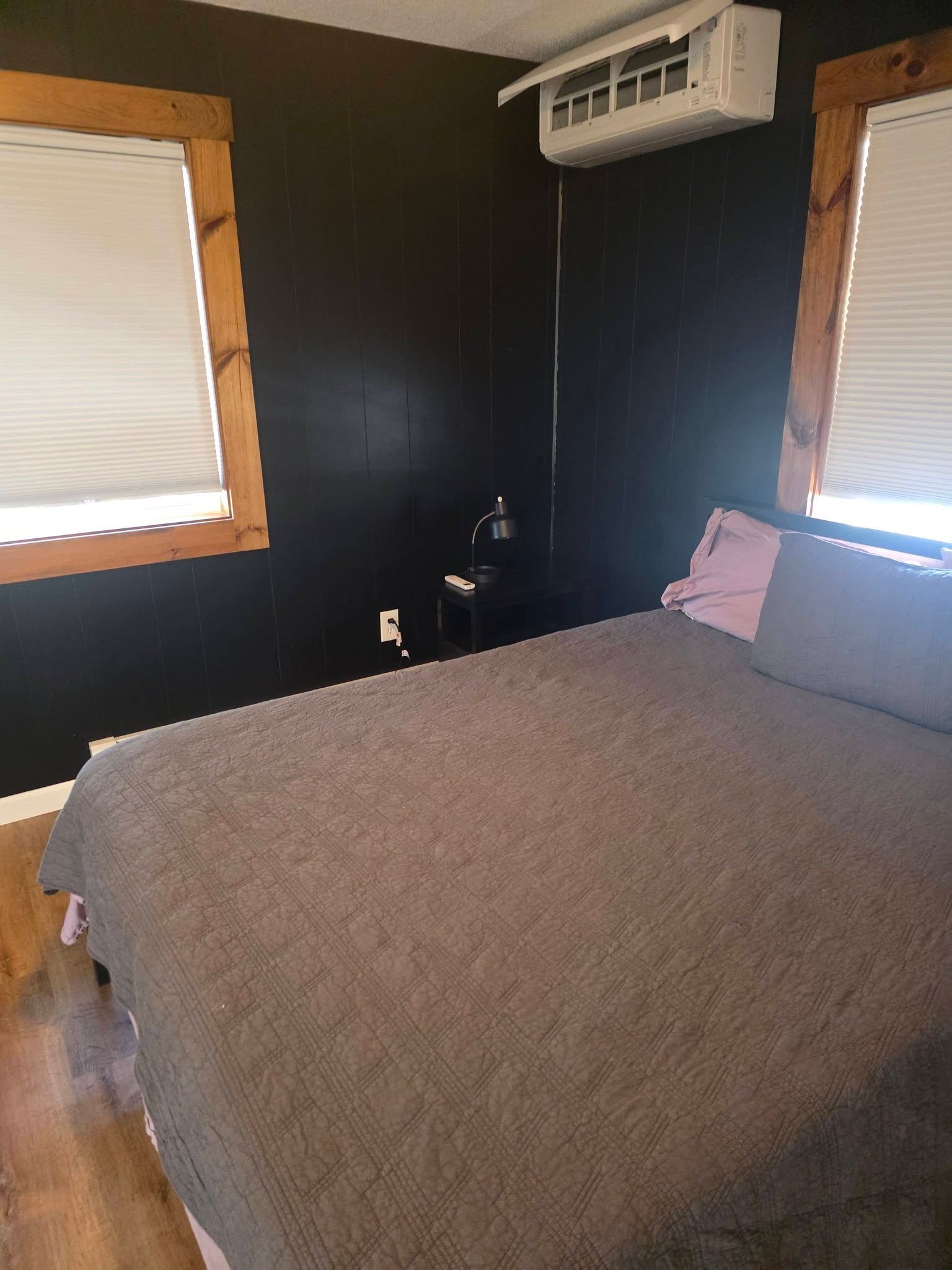 Small bedroom with black walls, two windows, a bed, and a wall-mounted air conditioner.