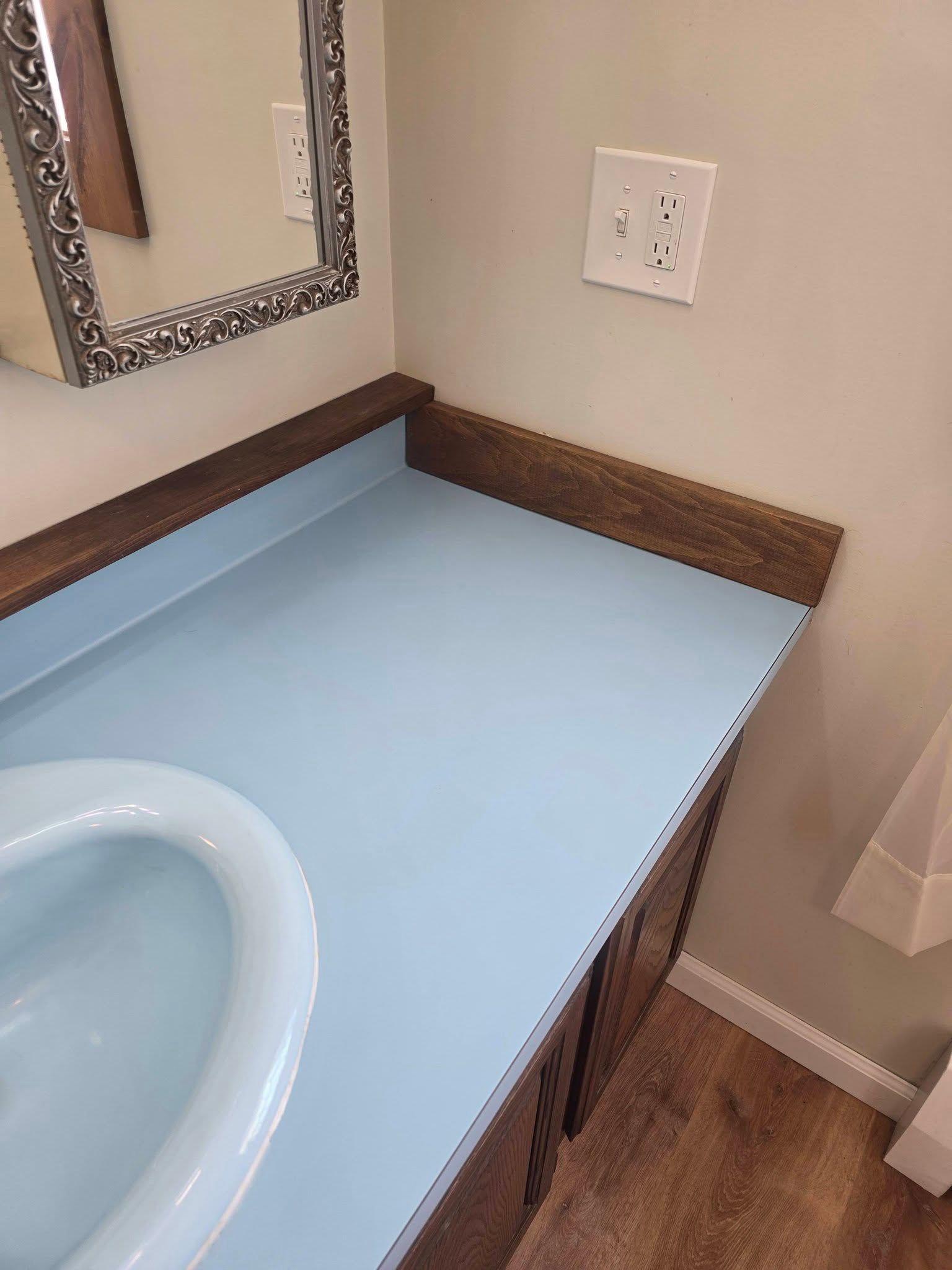 Bathroom vanity with light blue countertop, white sink, mirror, and wall outlet.