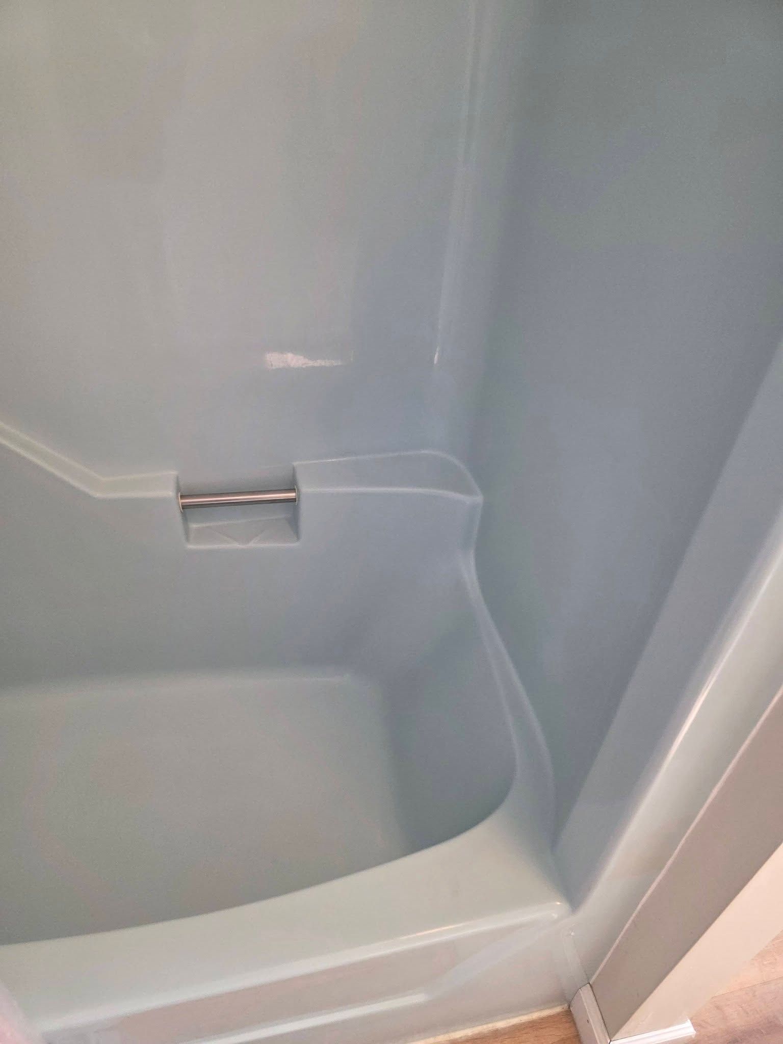 Close-up of a white bathtub corner with a built-in handle and shower wall surround.