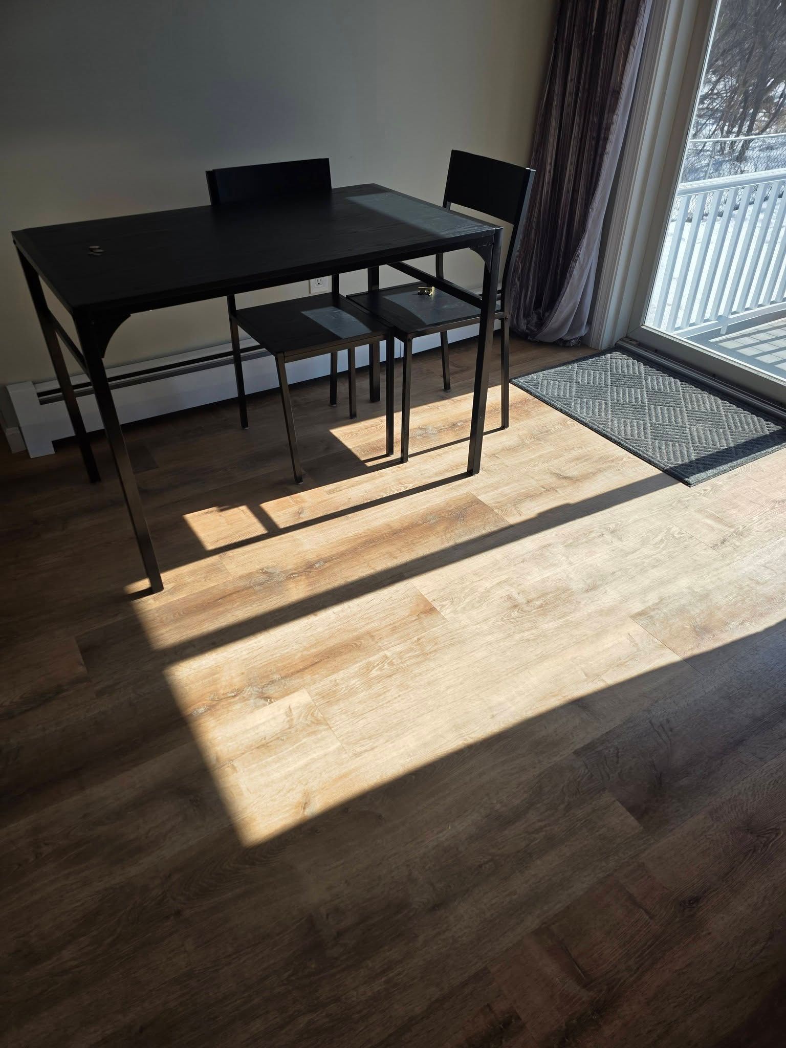 Dining table and chairs in a sunlit room with wooden floor and a door leading outside.