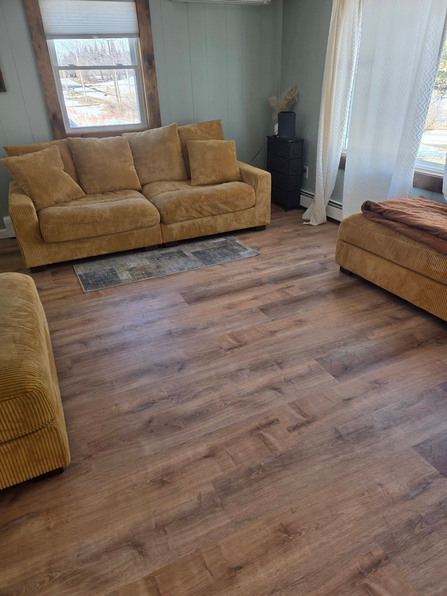 Living room with mustard sofa, wood floor, window, and sheer curtains