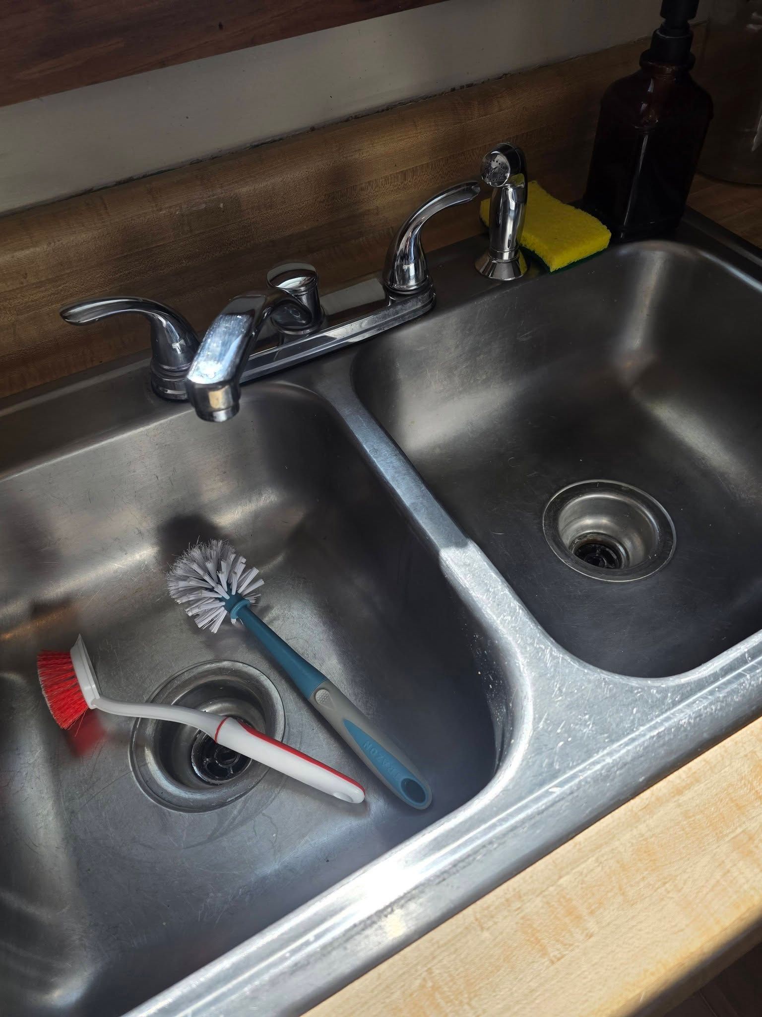Double kitchen sink with faucet and cleaning brush, one basin holding dishes and utensils