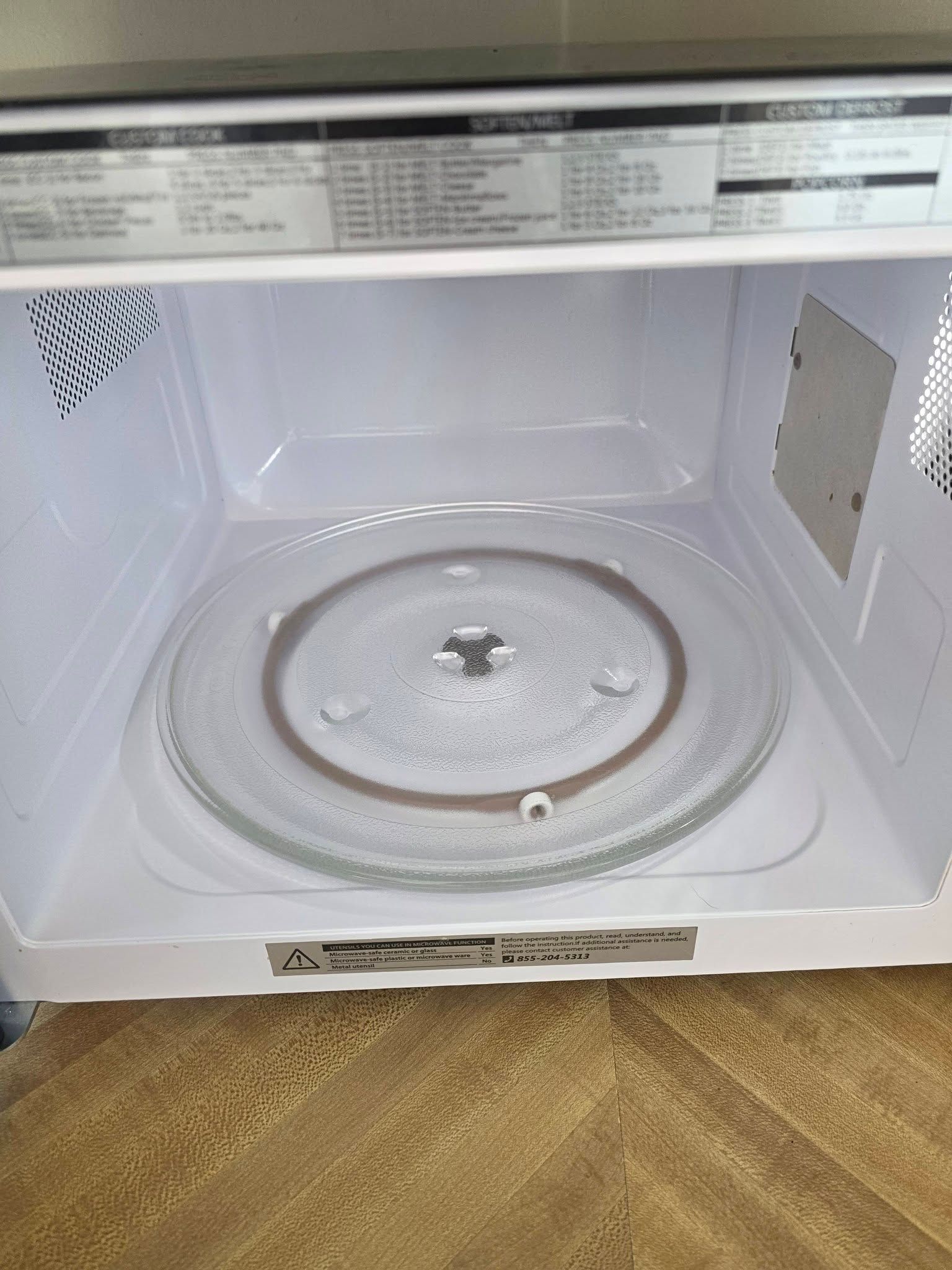 White microwave oven interior with glass turntable and open door, viewed from the front