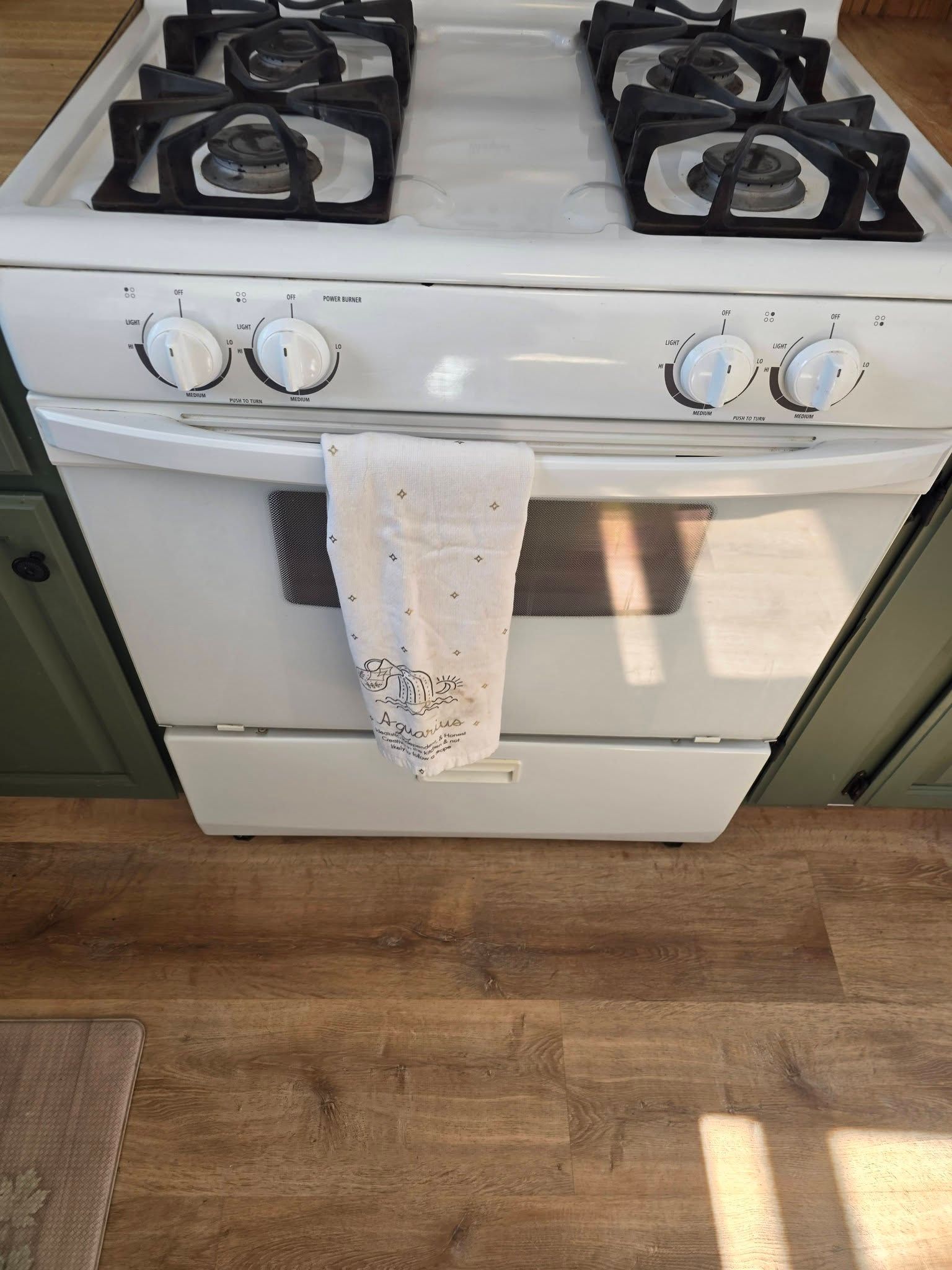 White gas stove with four burners and a hanging towel in a kitchen.