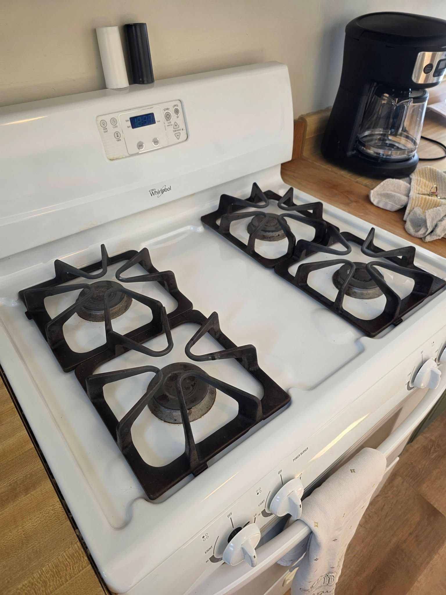 White gas stove with four burners on a kitchen counter, next to a black coffee maker and mugs.
