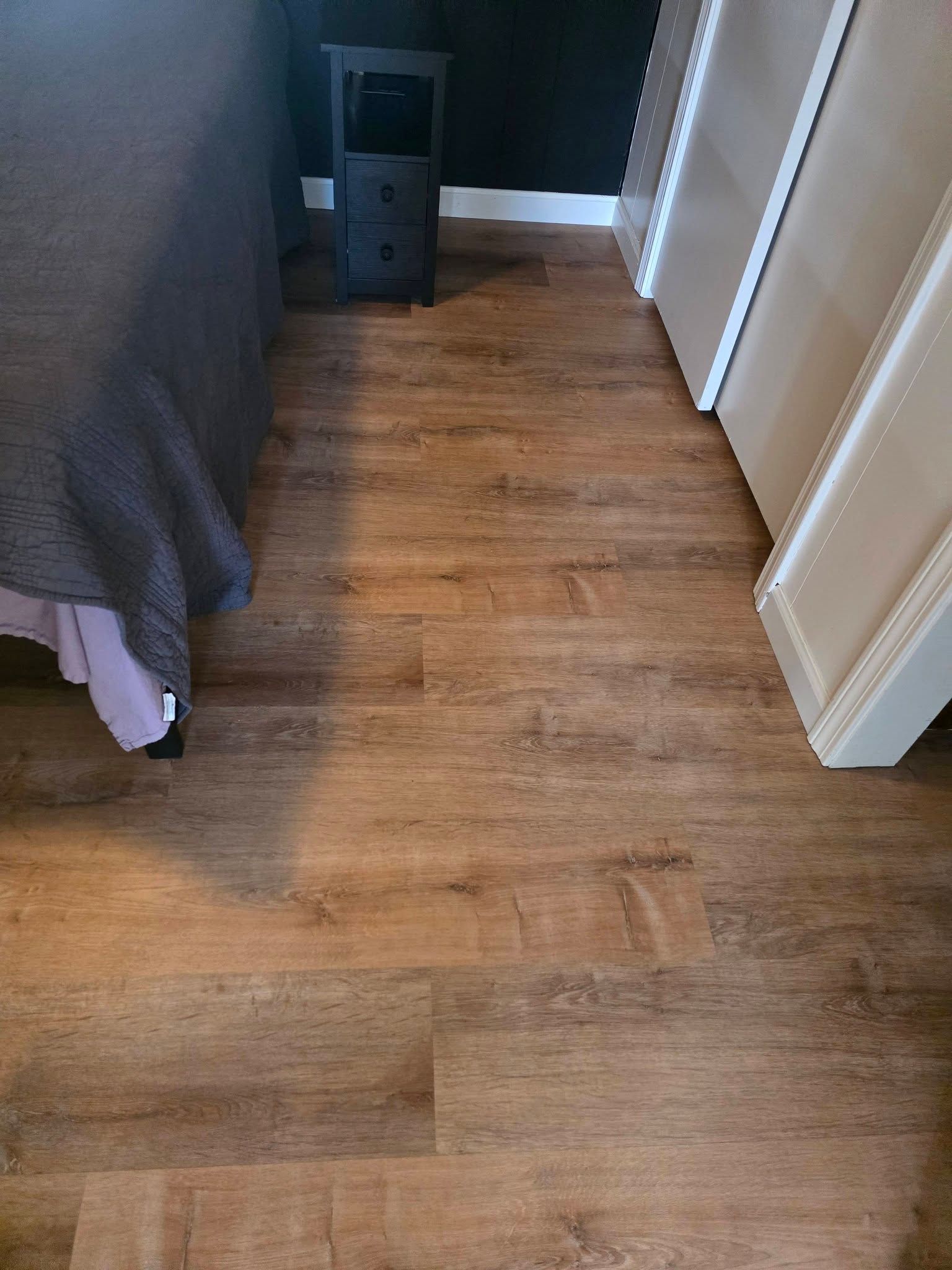 Wooden floor beside a bed and white wardrobe, with a black speaker against the wall.