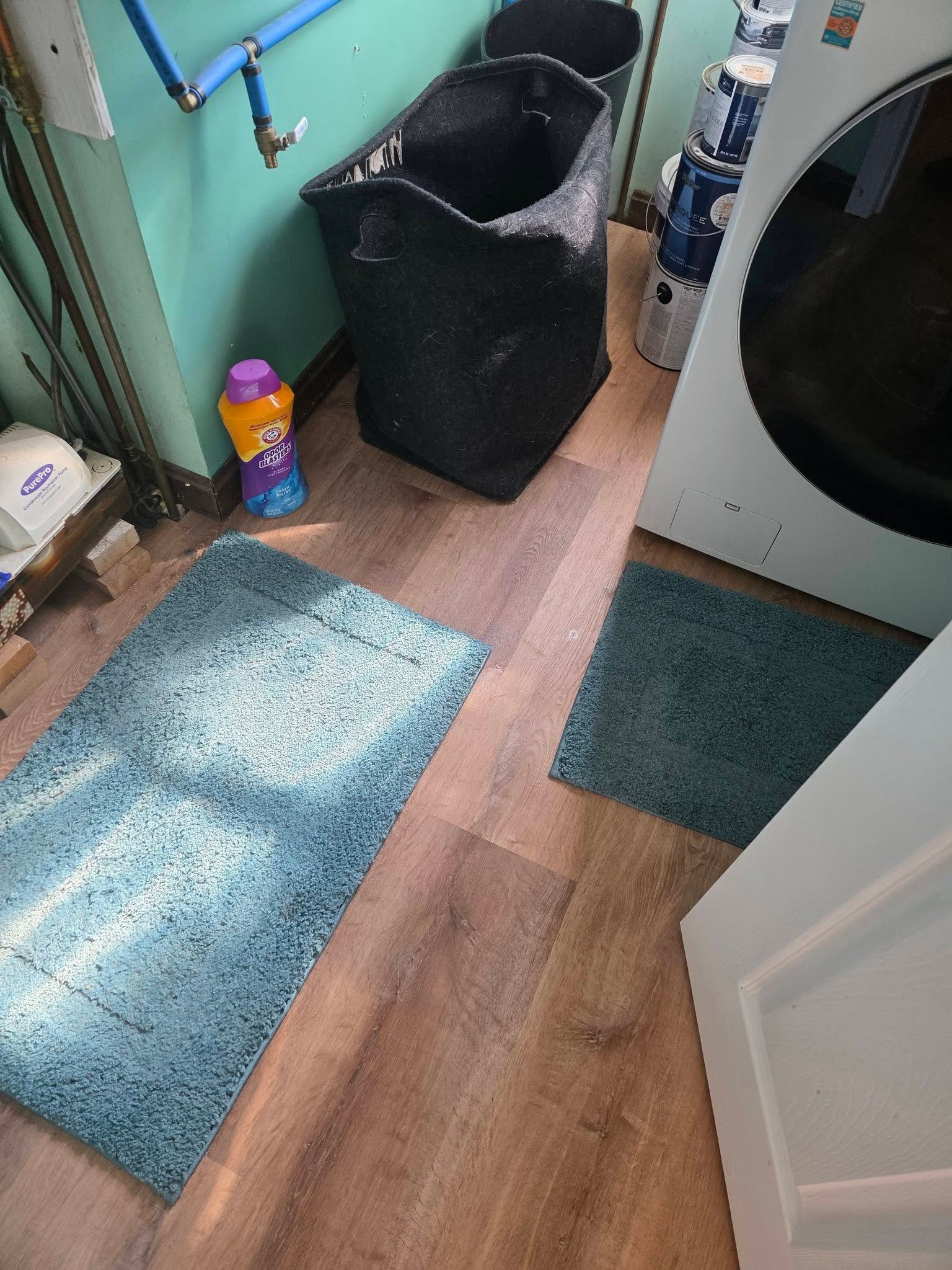 Bathroom with teal rugs, black laundry basket, and a washing machine beside a partially open door